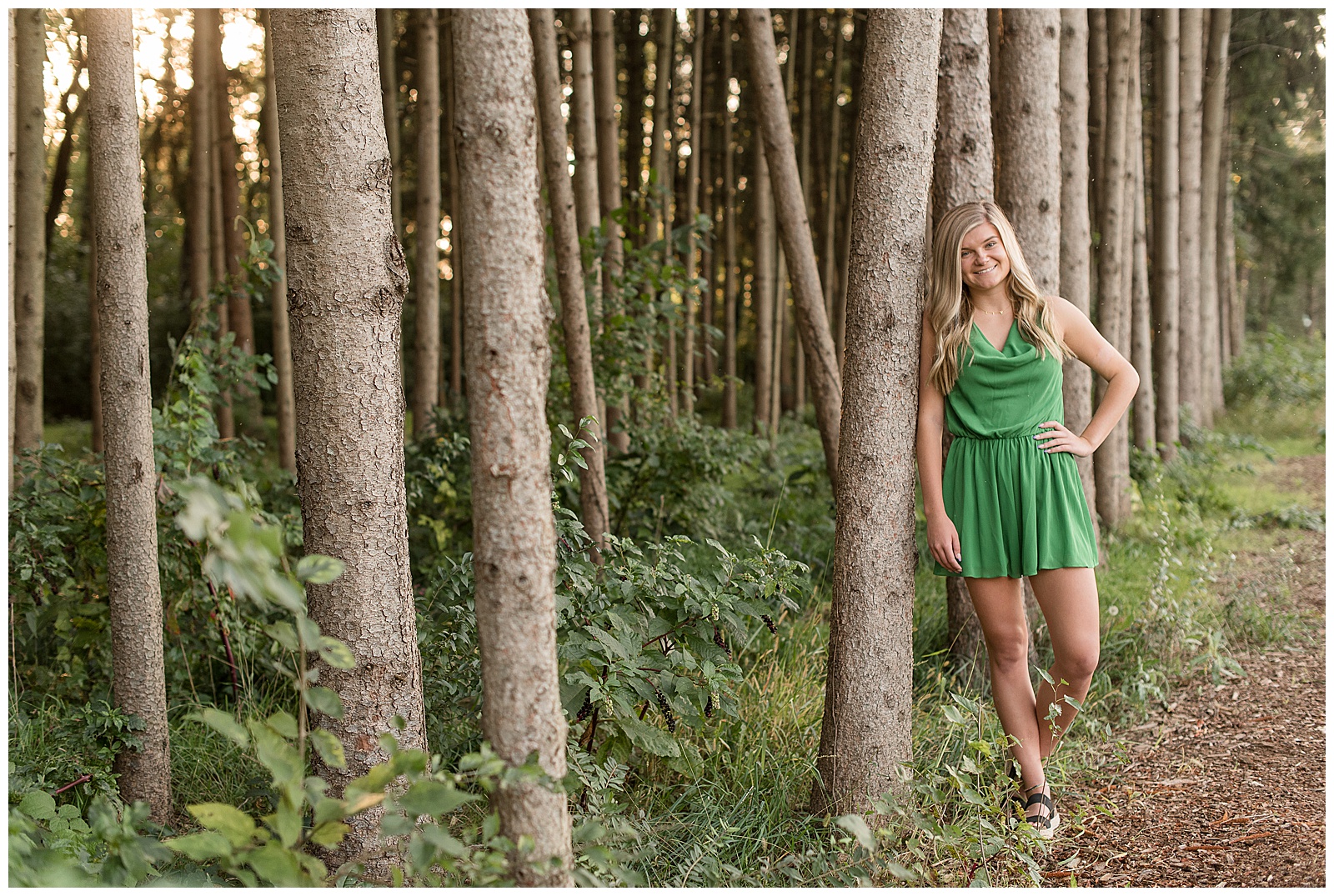 senior girl in green dress leaning right shoulder against pine tree with left hand on hip at overlook park