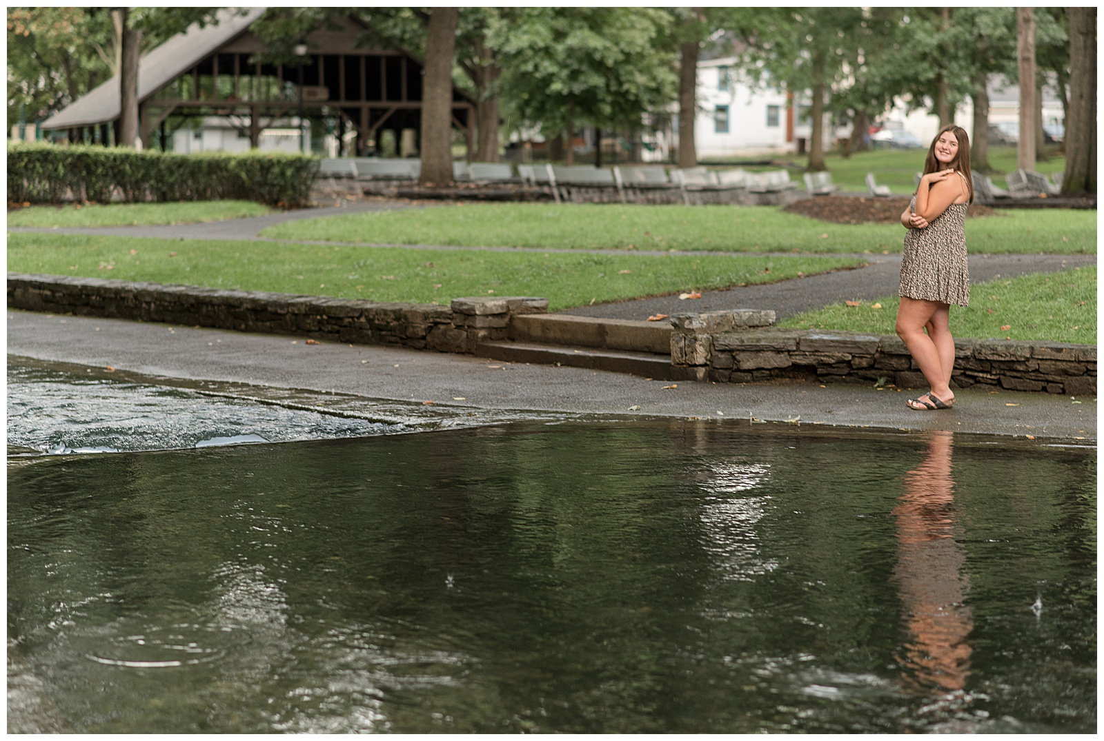 senior girl standing along pathway with right shoulder toward camera near water at lititz springs park