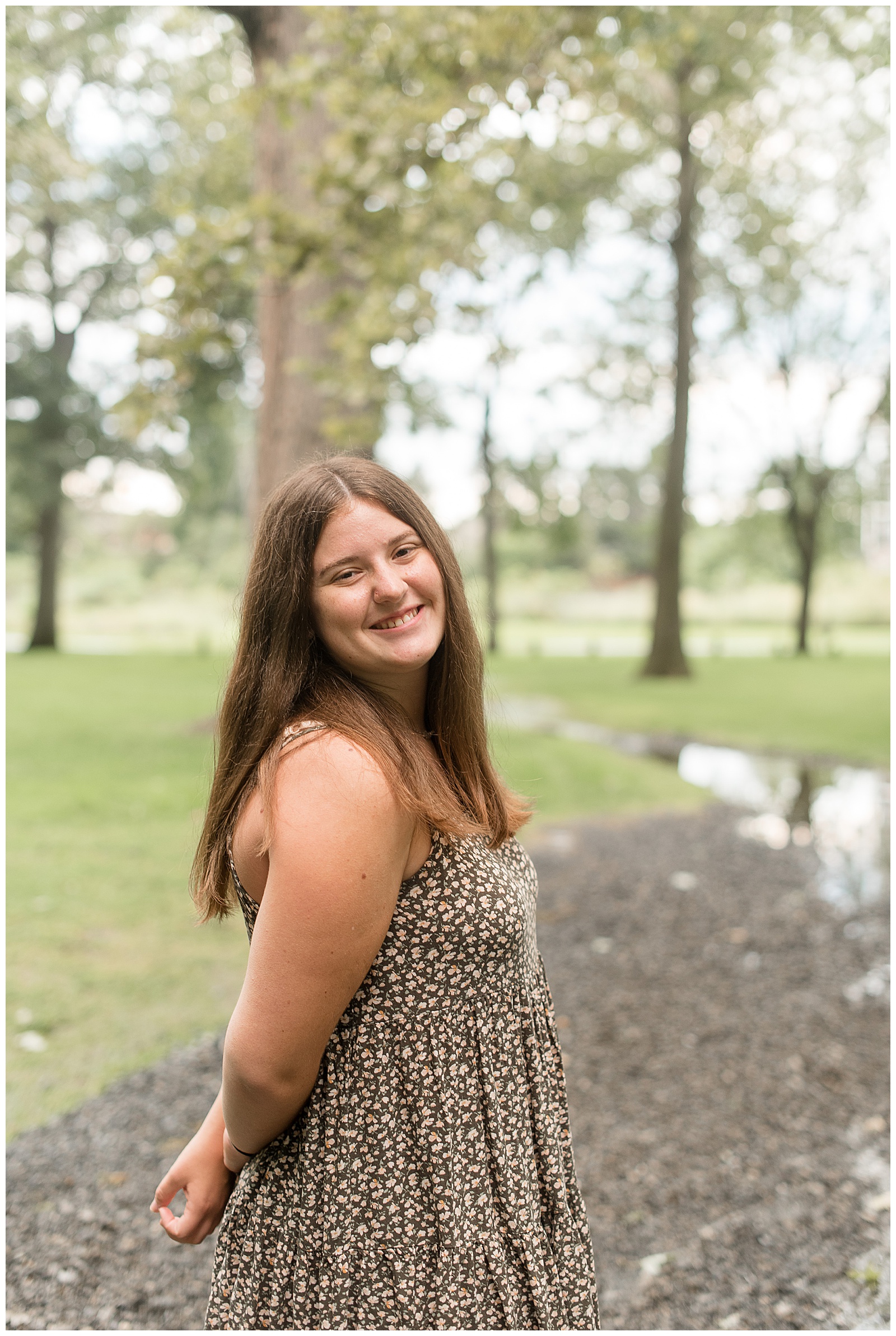 senior girl smiling with her right shoulder towards camera and her hands joined behind her back along stone path at lititz springs park