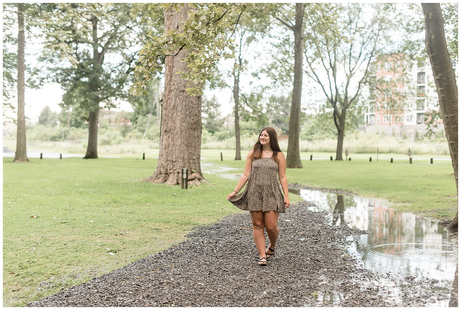 senior girl walking along stone path by puddles on rainy evening as she holds the edges of her dress in lititz