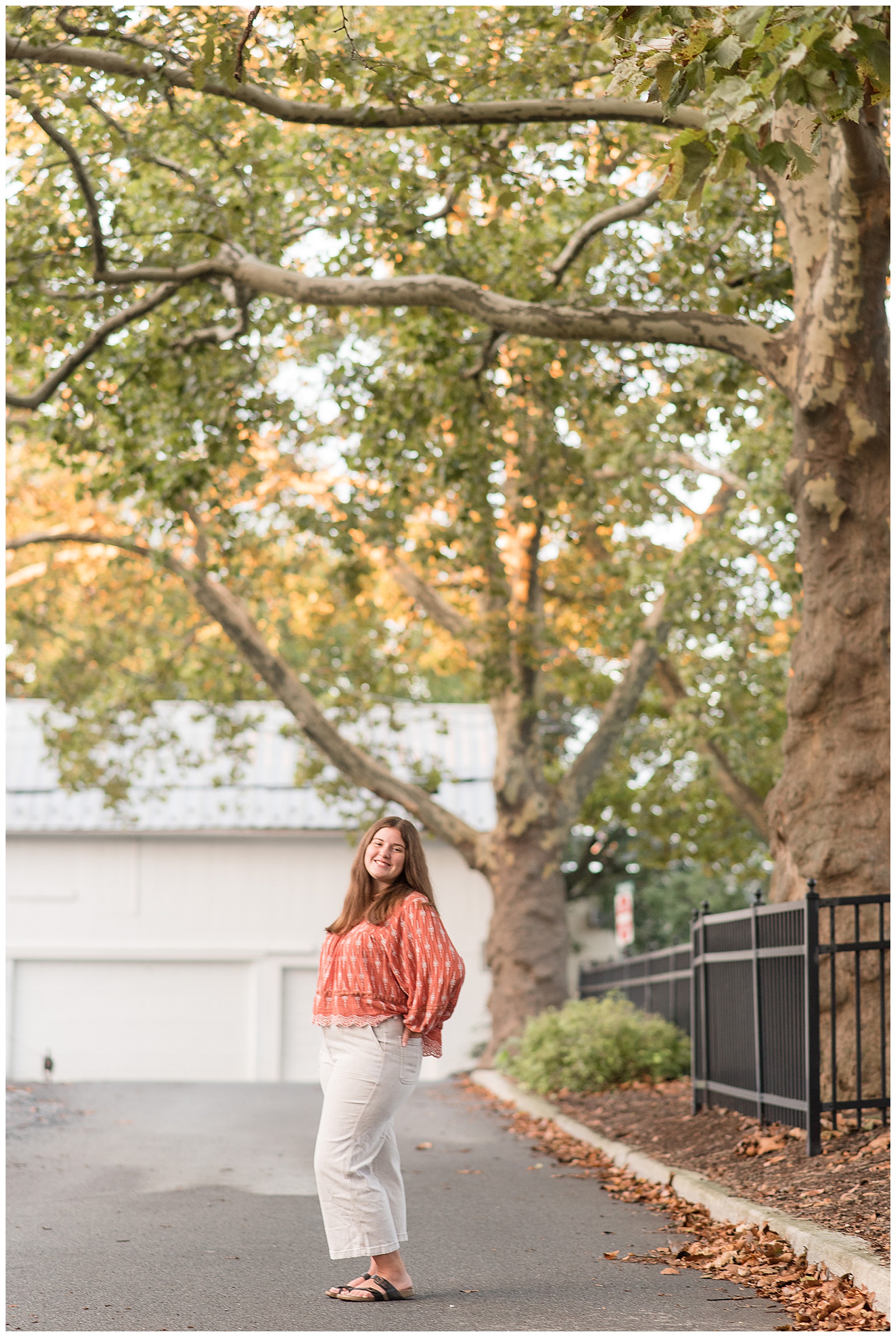senior girl standing in road with left side angled toward camera by black iron fence and tree in downtown lititz pennsylvania