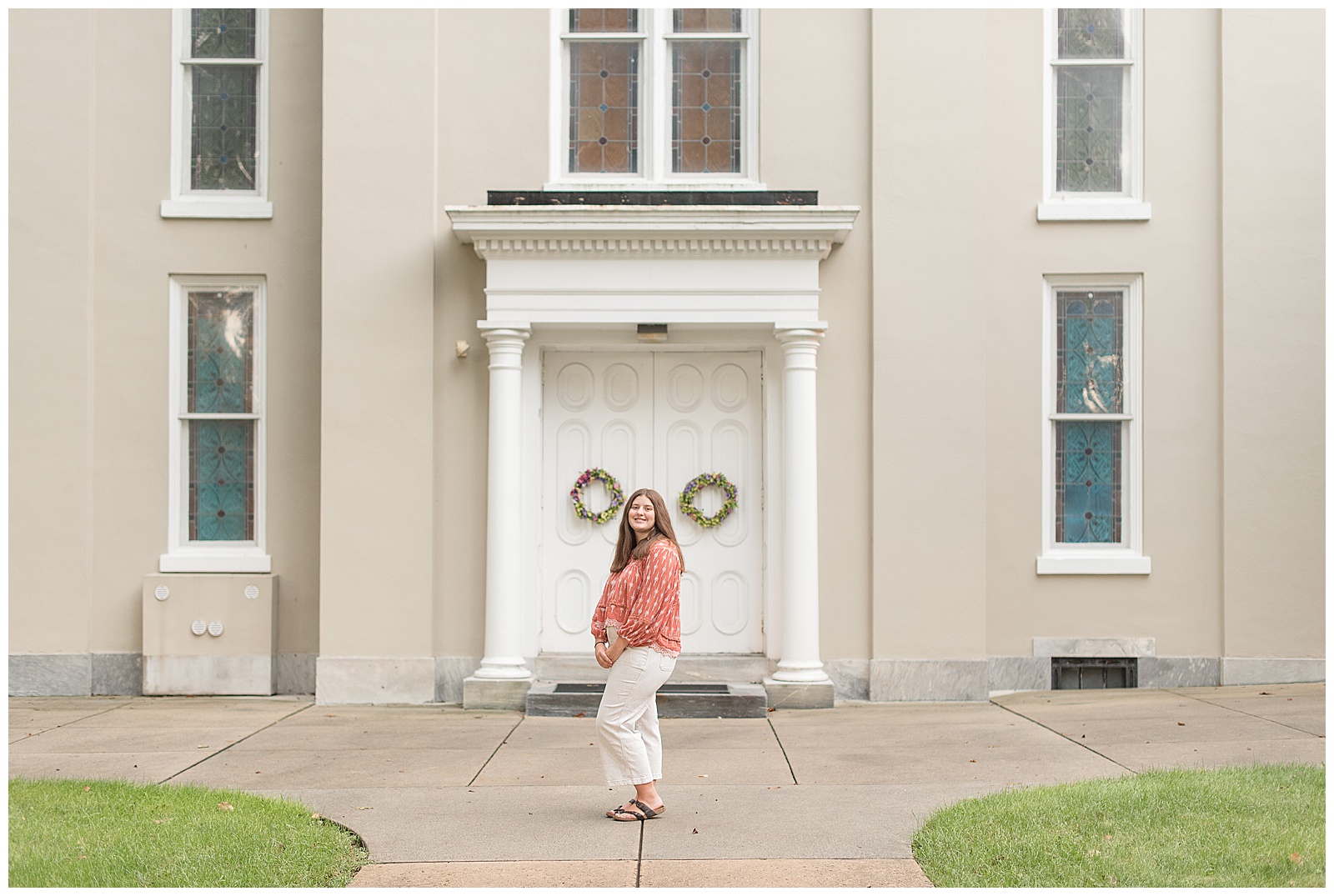 senior girl in front of tan building with white doors and white columns with left side angled toward camera in lititz pennsylvania