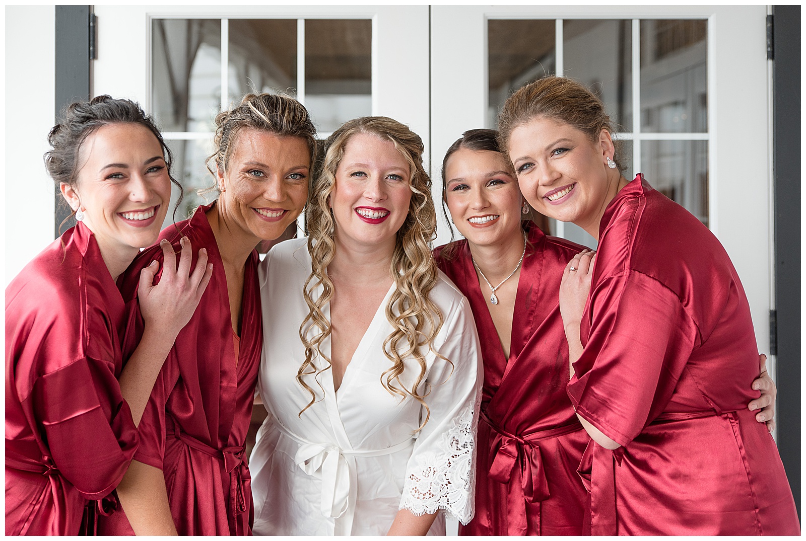 bride surrounded by her bridesmaids as they all wearing silky robes while getting ready in the bridal suite at the barn at silverstone