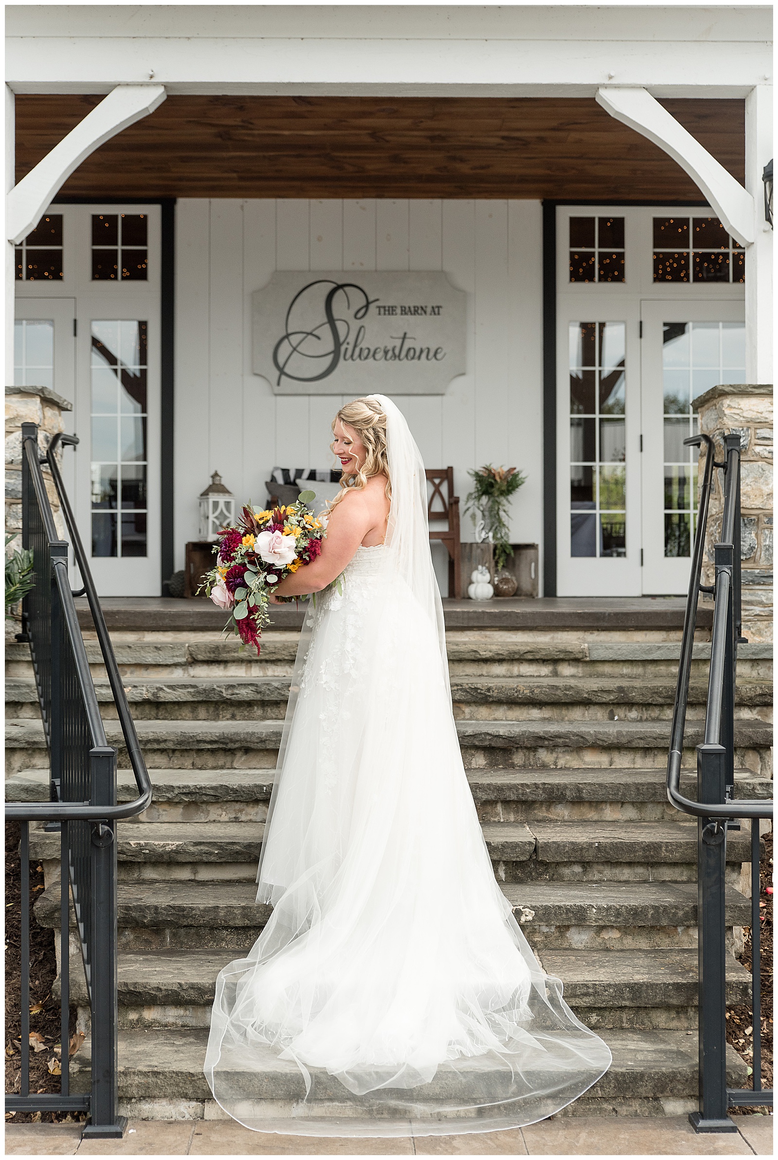 bride standing on staircase with back toward camera looking back over left shoulder holding fall bouquet at the barn at silverstone