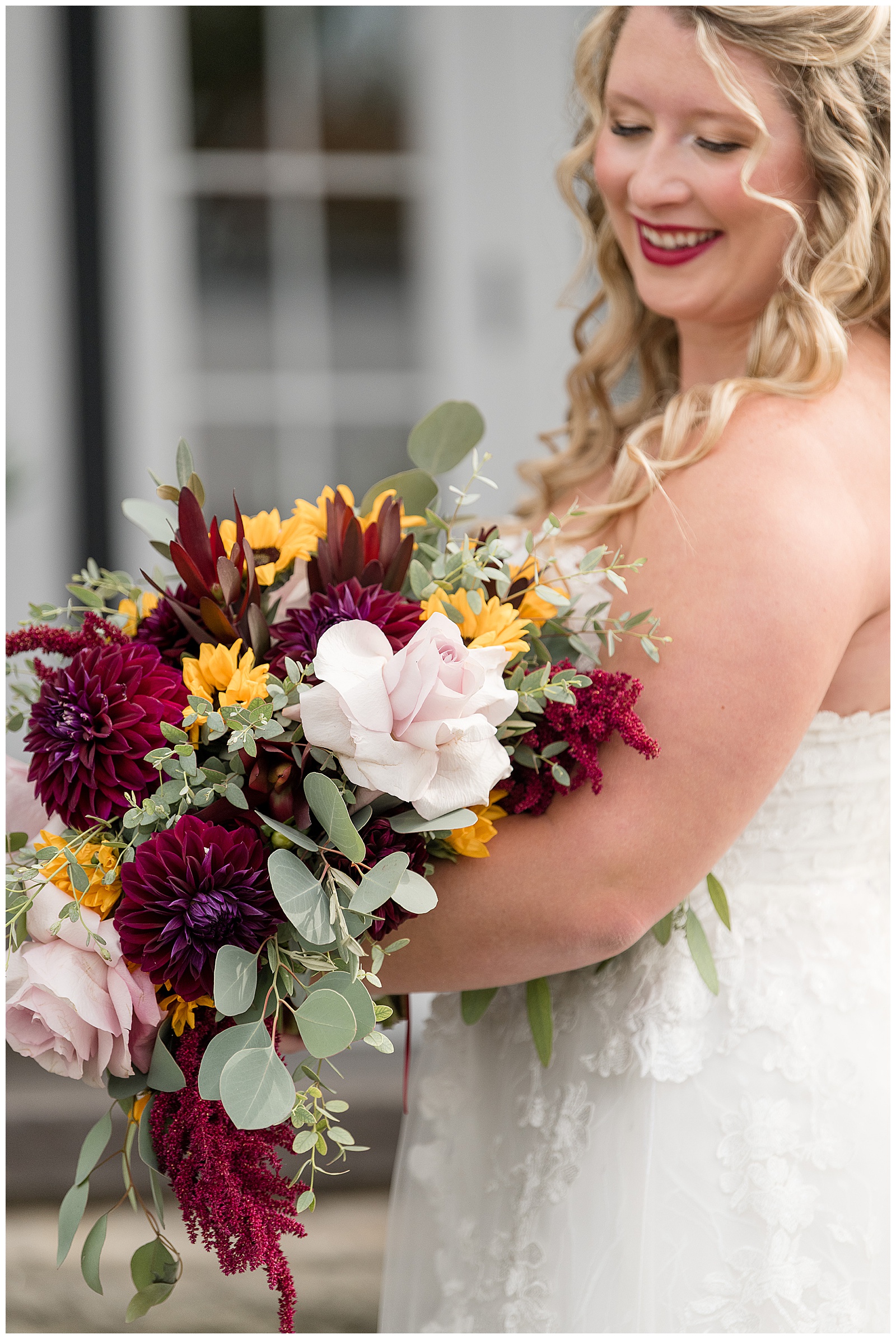 bride holding beautiful fall flower bouquet filled with sunflowers and dark red dahlias at the barn at silverstone