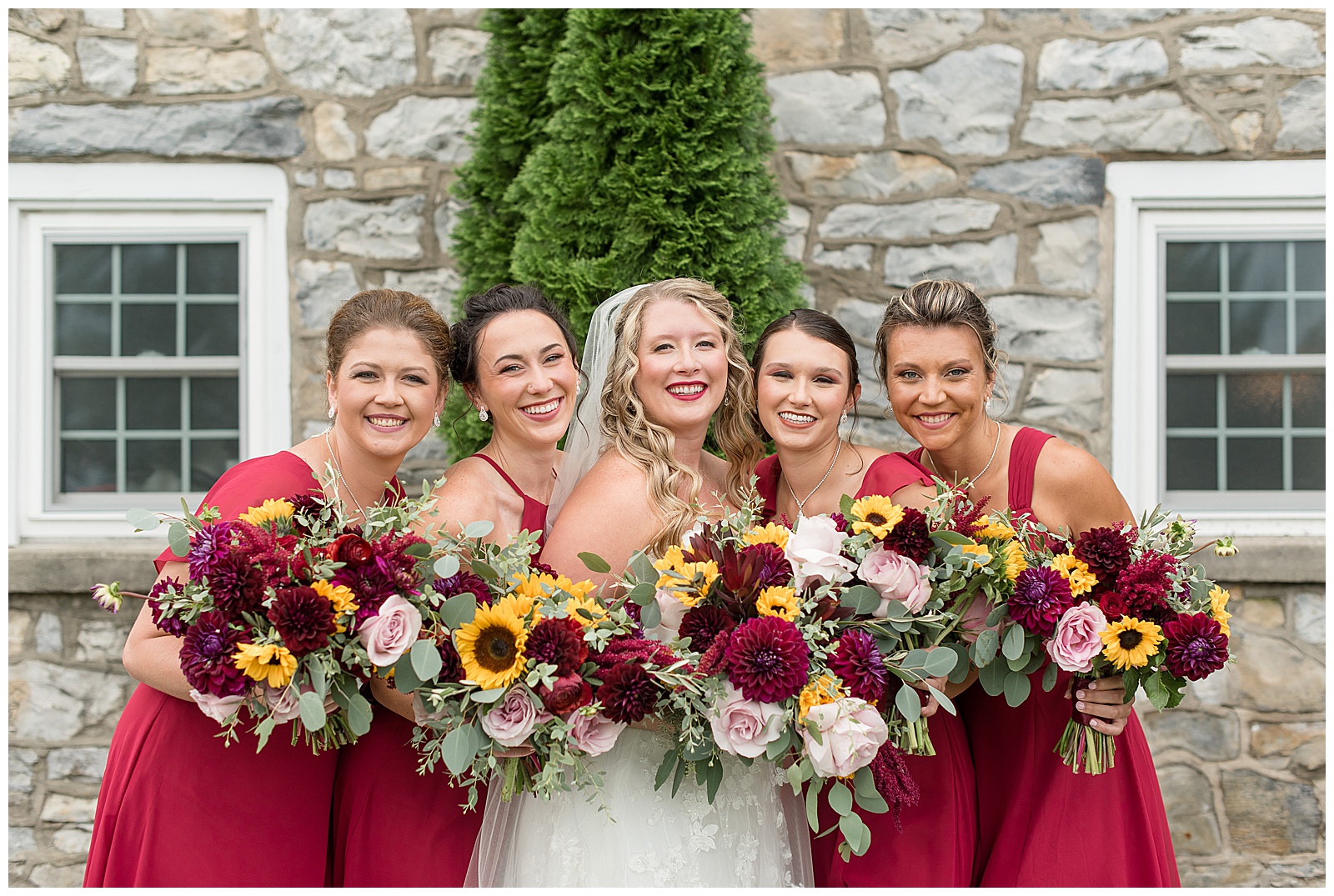 bride and her bridesmaids standing close together and holding their bouquets as they smile and look at camera at the barn at silverstone