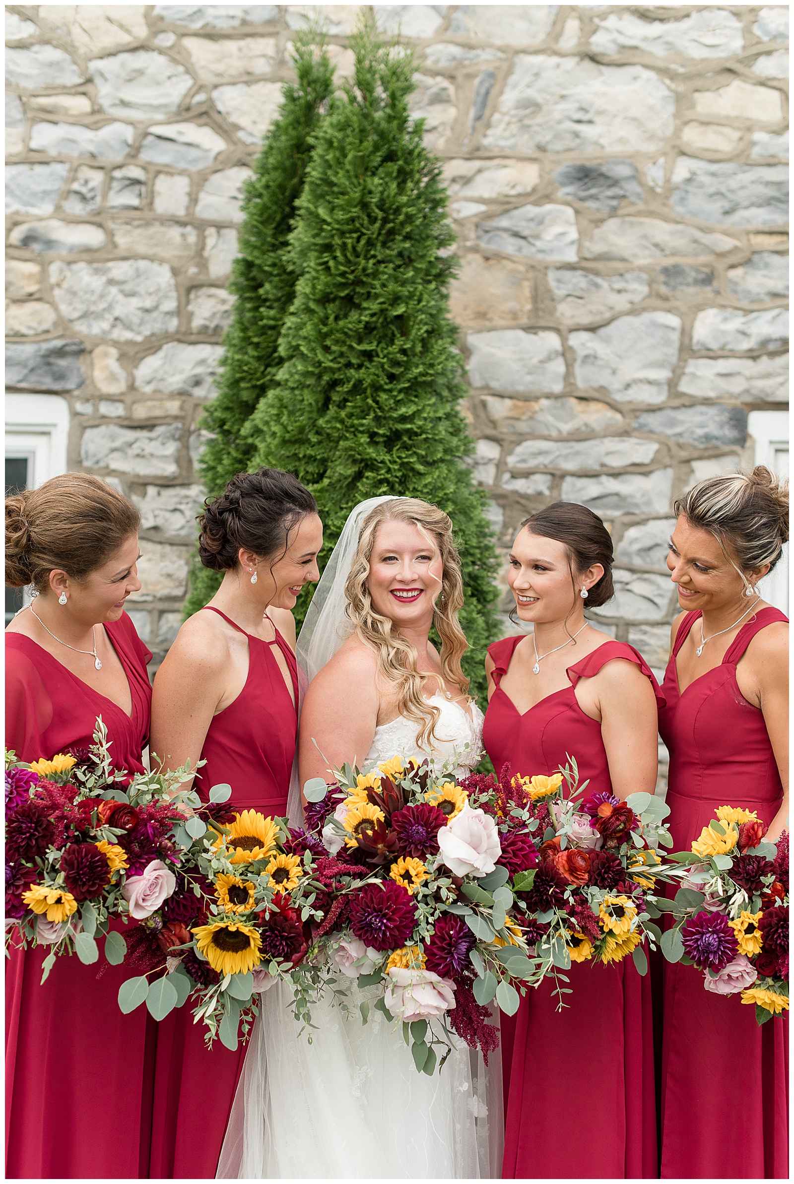 bride in strapless white wedding gown and bridesmaids wearing red dresses a smiling at the barn at silverstone