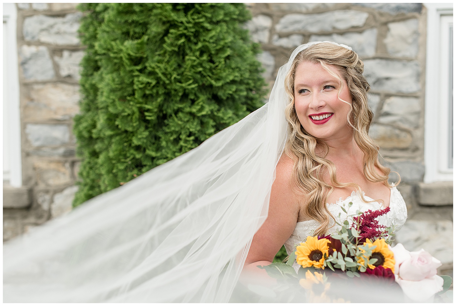 bride looking out over her right shoulder and into the distance with veil blowing behind her as she holds fall bouquet in lancaster pennsylvania
