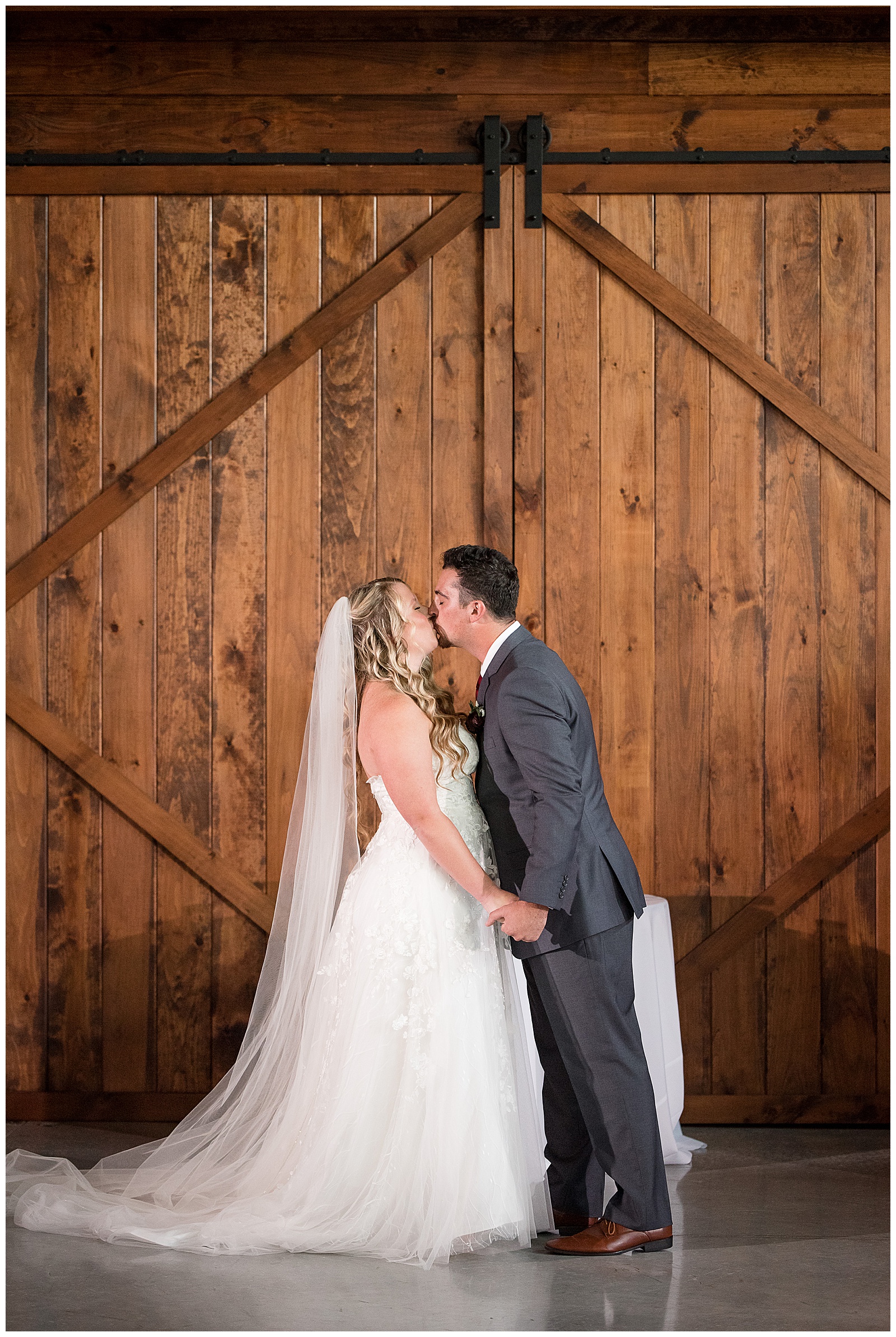 bride and groom share their first kiss as husband and wife during wedding ceremony by wooden barn doors in lancaster pennsylvania