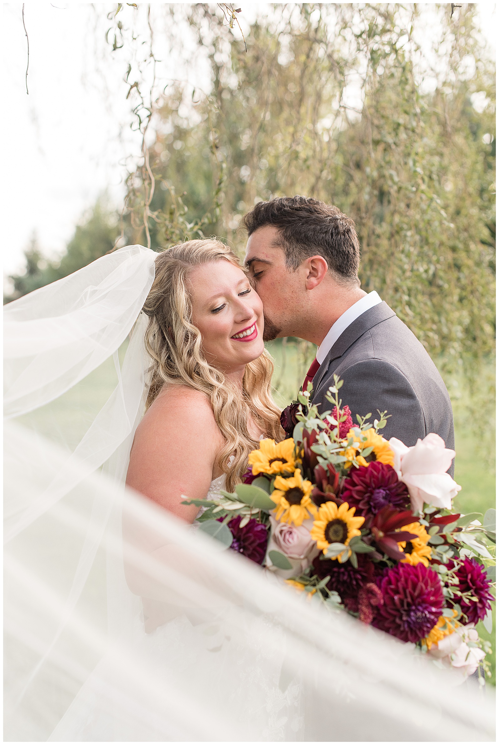 groom kissing bride's left cheek as she smiles and looks down and holds fall bouquet at the barn at silverstone