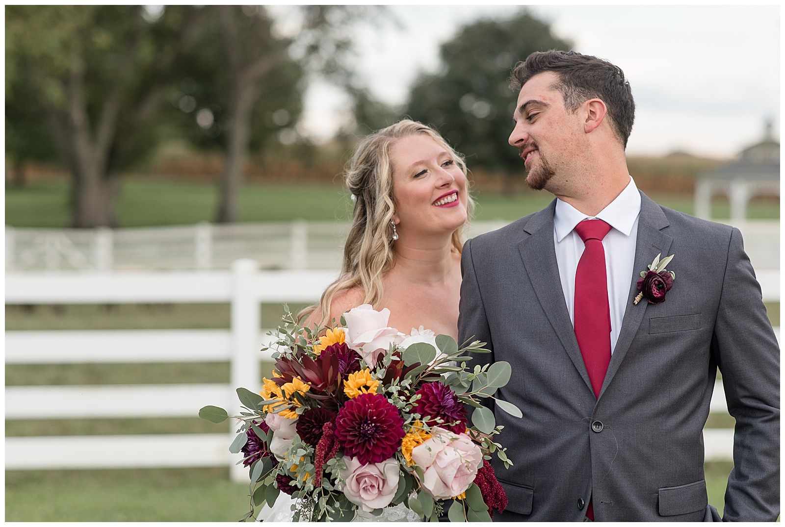 bride holding fall bouquet in right hand with her left hand wrapped around groom's right arm as they both smile and look at each other in lancaster pennsylvania