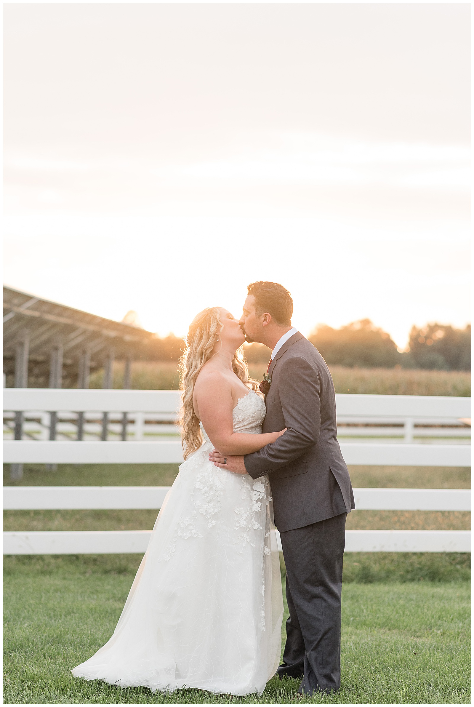 couple kissing with the sun setting and a white fence behind them at the barn at silverstone