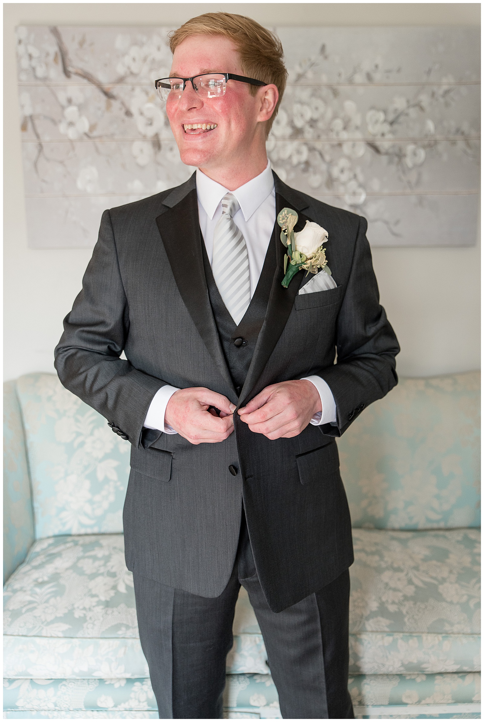 groom looking over right shoulder smiling as he buttons up his black suit coat at cameron estate inn in lancaster pennsylvania