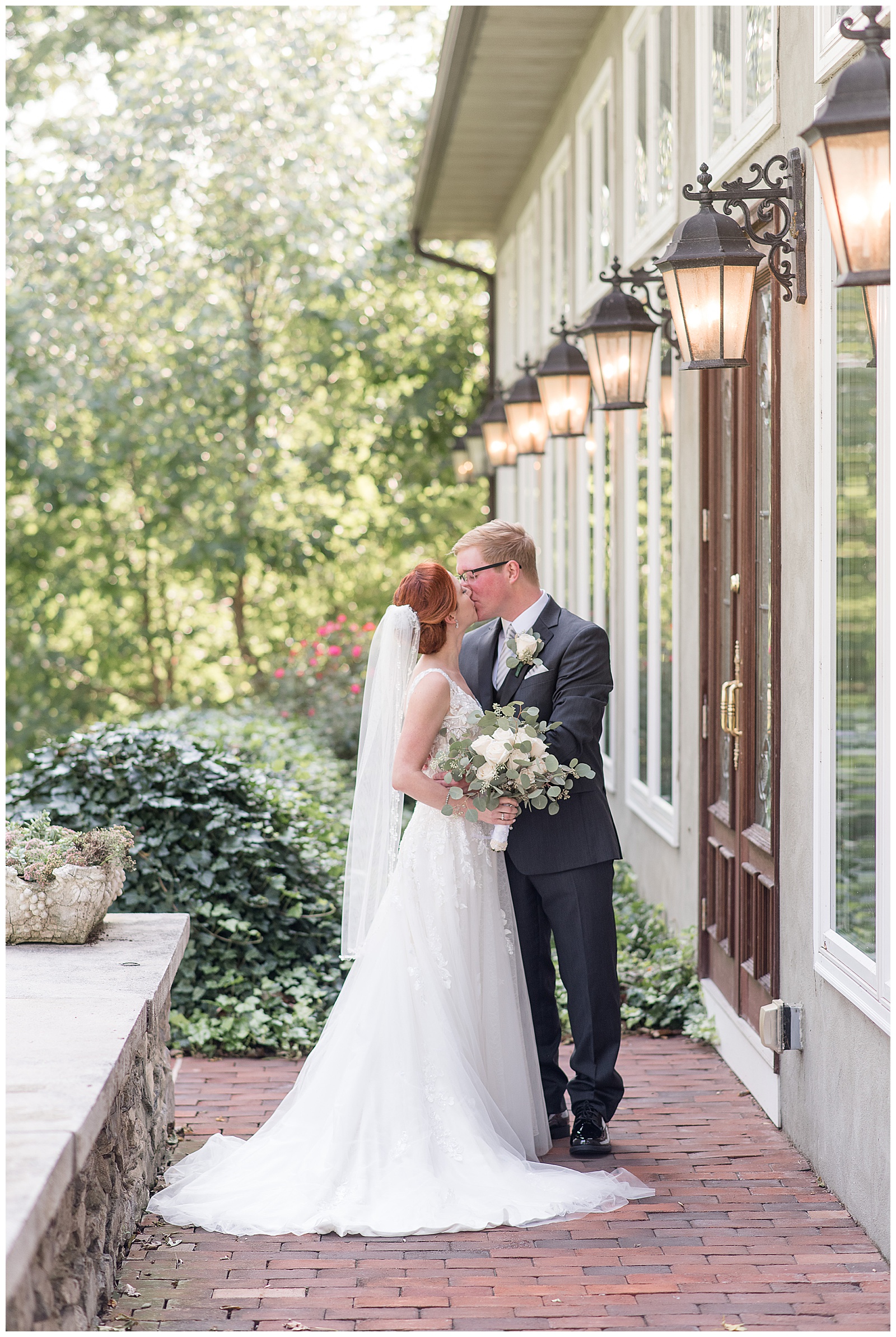 bride and groom hug and kiss outside home at cameron estate inn with beautiful landscaping behind them