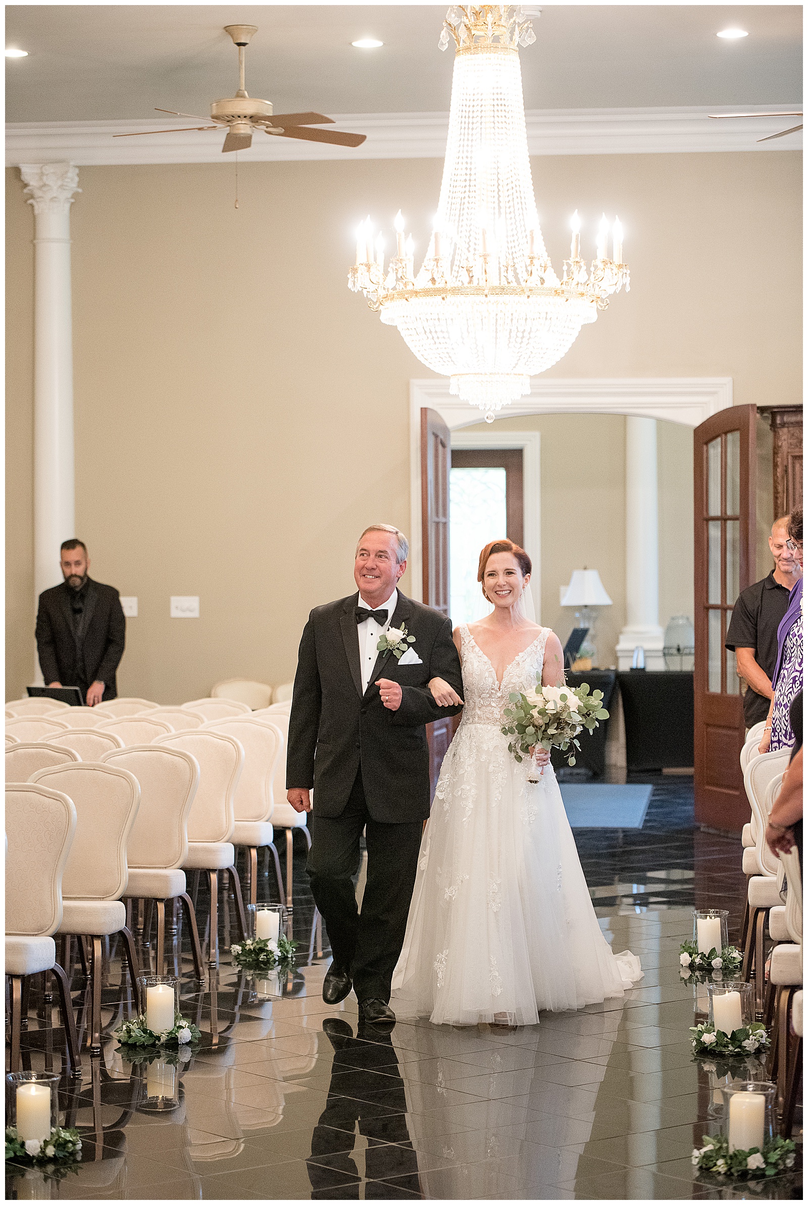 bride and her father walking down the aisle during indoor wedding ceremony with chandelier above them at cameron estate inn