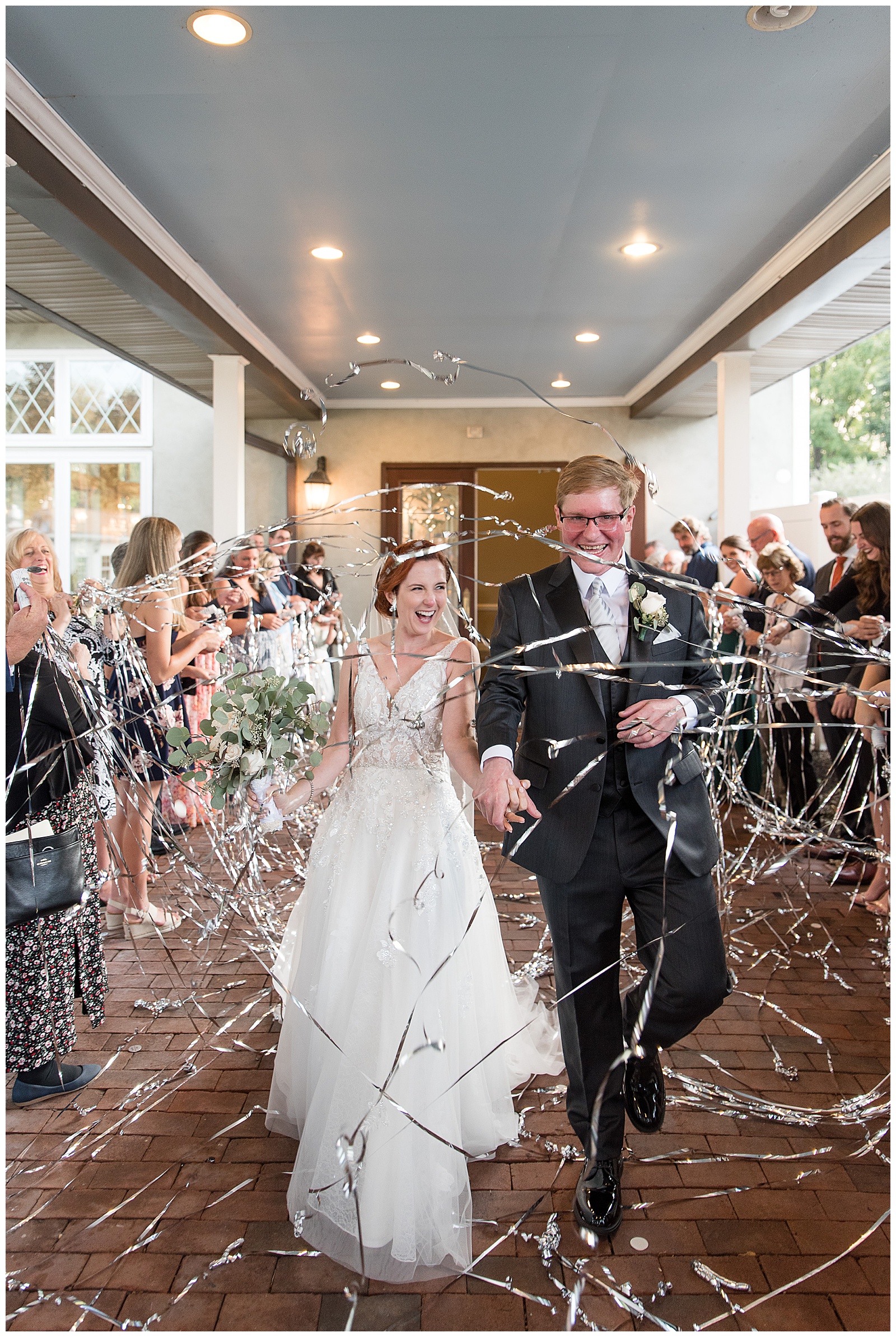 bride and groom walking through sea of confetti as they exit ceremony surrounded by their guests on summer day