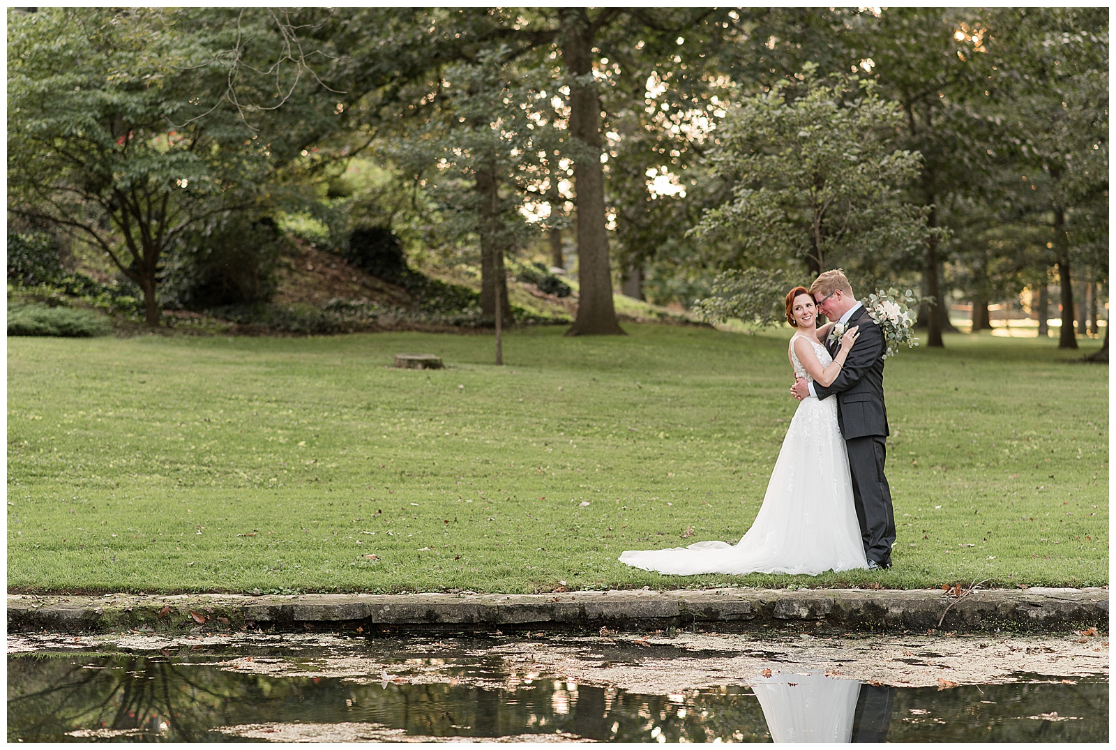 bride and groom hugging in lawn with trees behind them and pond in front of them at cameron estate inn