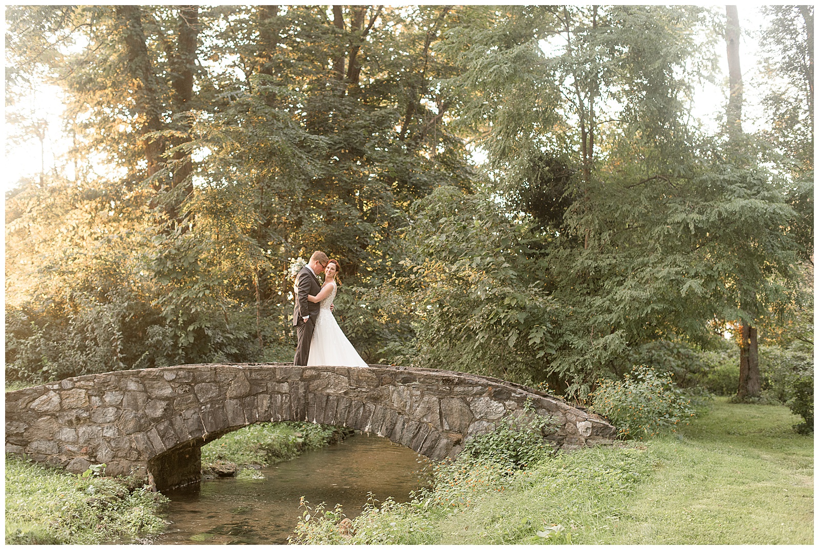 bride and groom hugging while standing in the middle of beautiful stone bridge with stream below them at cameron estate inn in lancaster pennsylvania