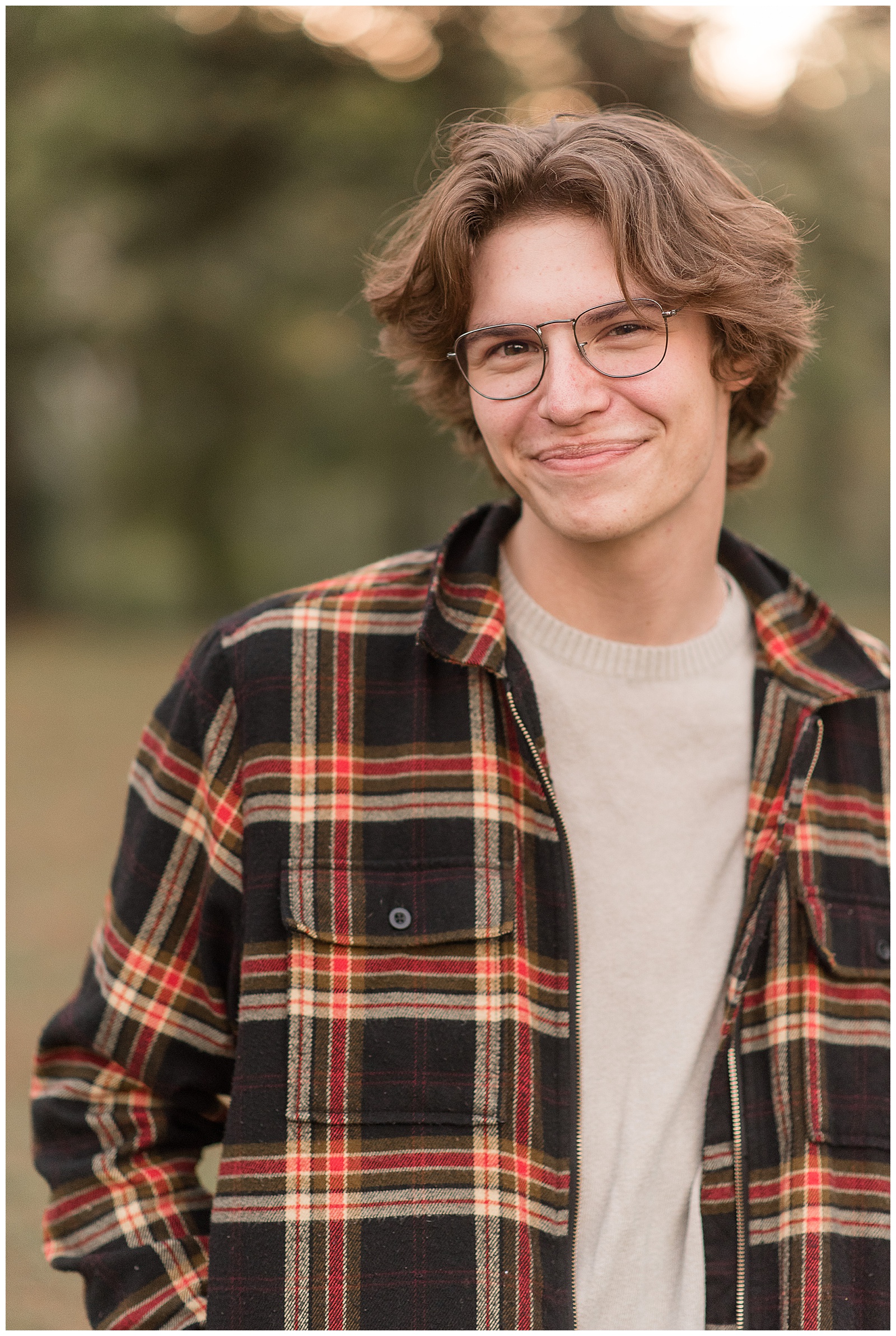 close up of senior guy smiling at camera wearing flannel shirt with hands in pockets at lancaster county park