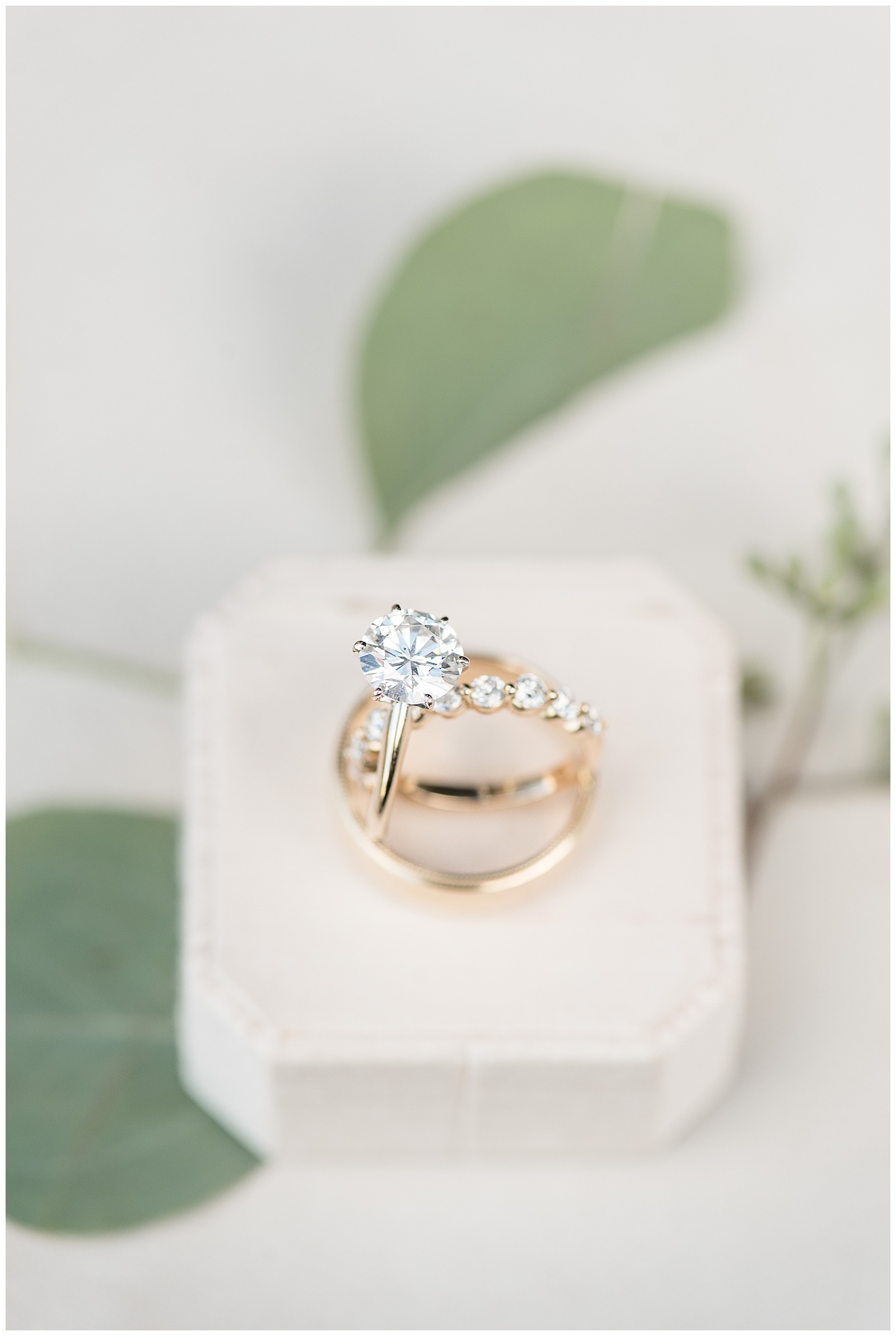 diamond engagement ring and diamond wedding band on display in ivory jewelry box with eucalyptus in background in new jersey
