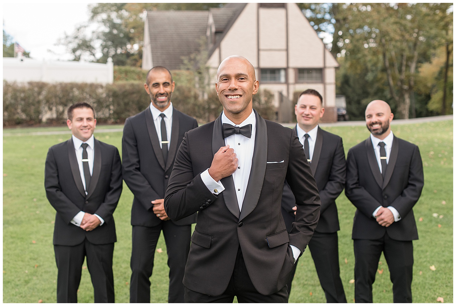 groom holding edge of his black suit coat and smiling with his four groomsmen all standing behind him at north jersey country club