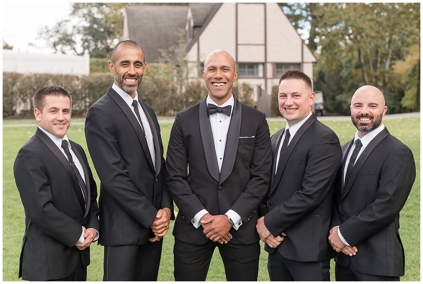 groom with two groomsmen on each side of him with their hands folding in front of them and house behind them in new jersey