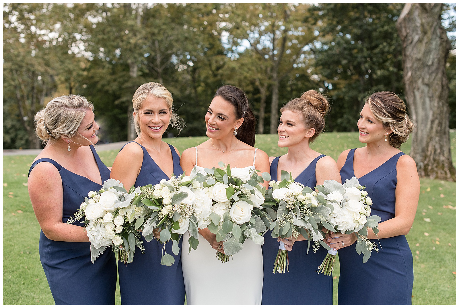 bride and bridesmaids all looking at each other smiling and standing close together holding bouquets at north jersey country club
