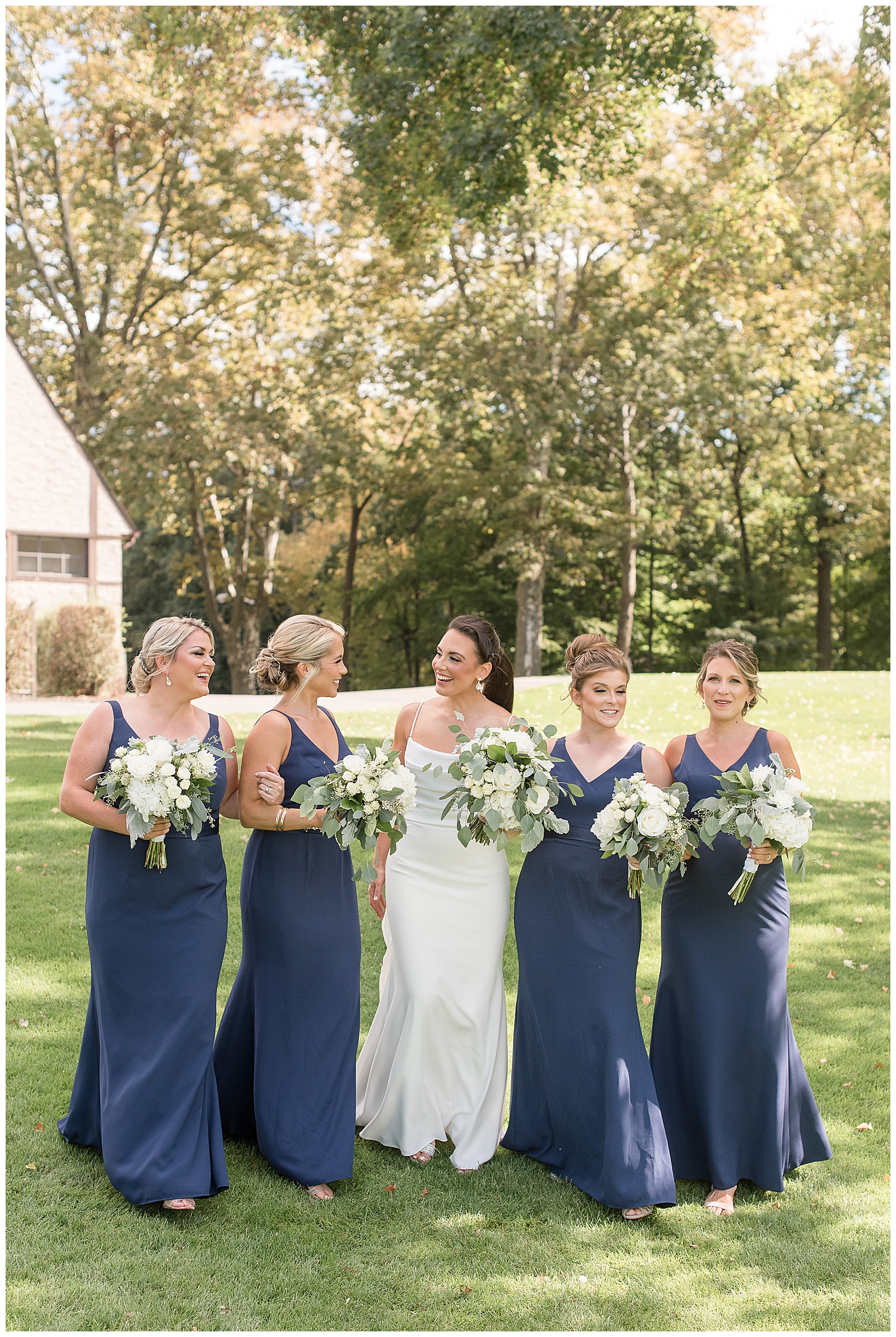 bride and bridesmaids all looking at each other slowly walking towards camera as they hold their bouquets on sunny fall day in new jersey