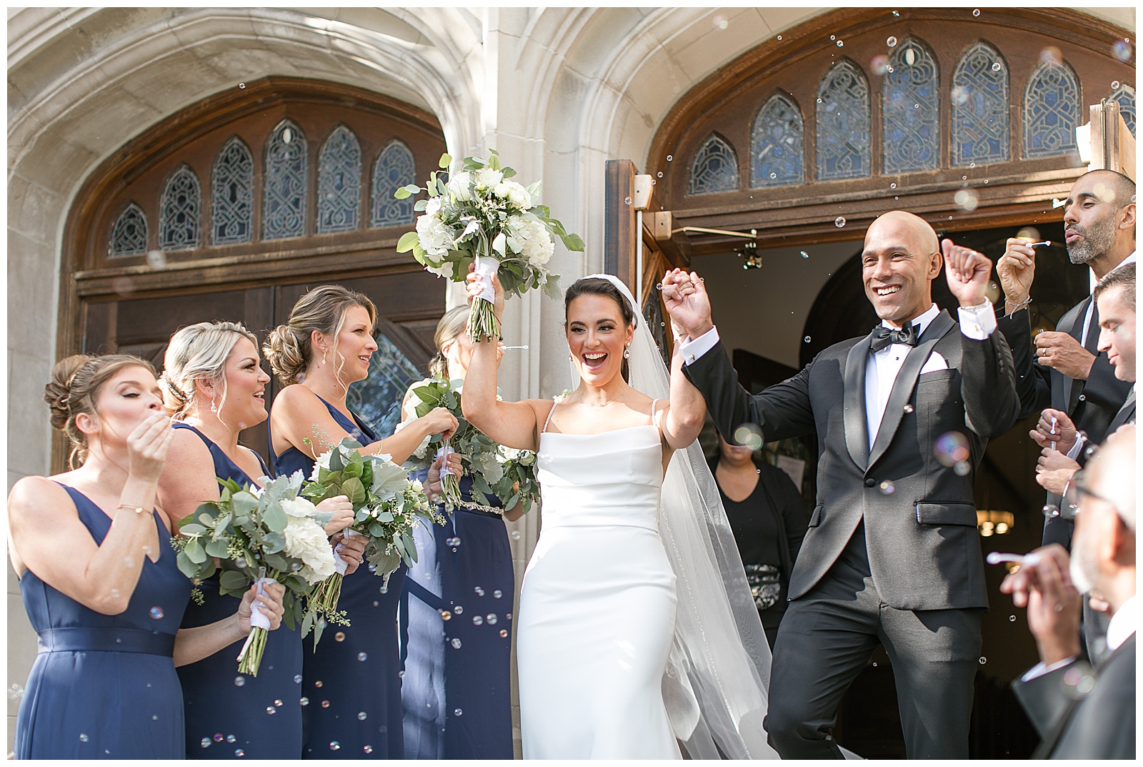 bride and groom rejoice with arms up surrounded by their wedding party as they leave the catholic church in new jersey