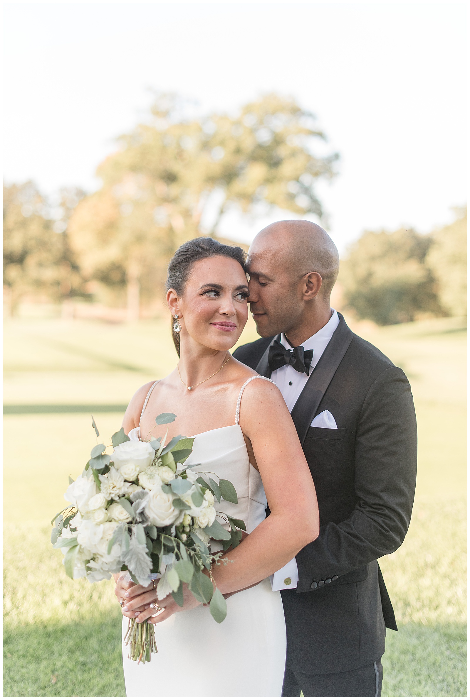 groom standing behind bride with his forehead resting against her left temple as they both smile standing on golf course at north jersey country club
