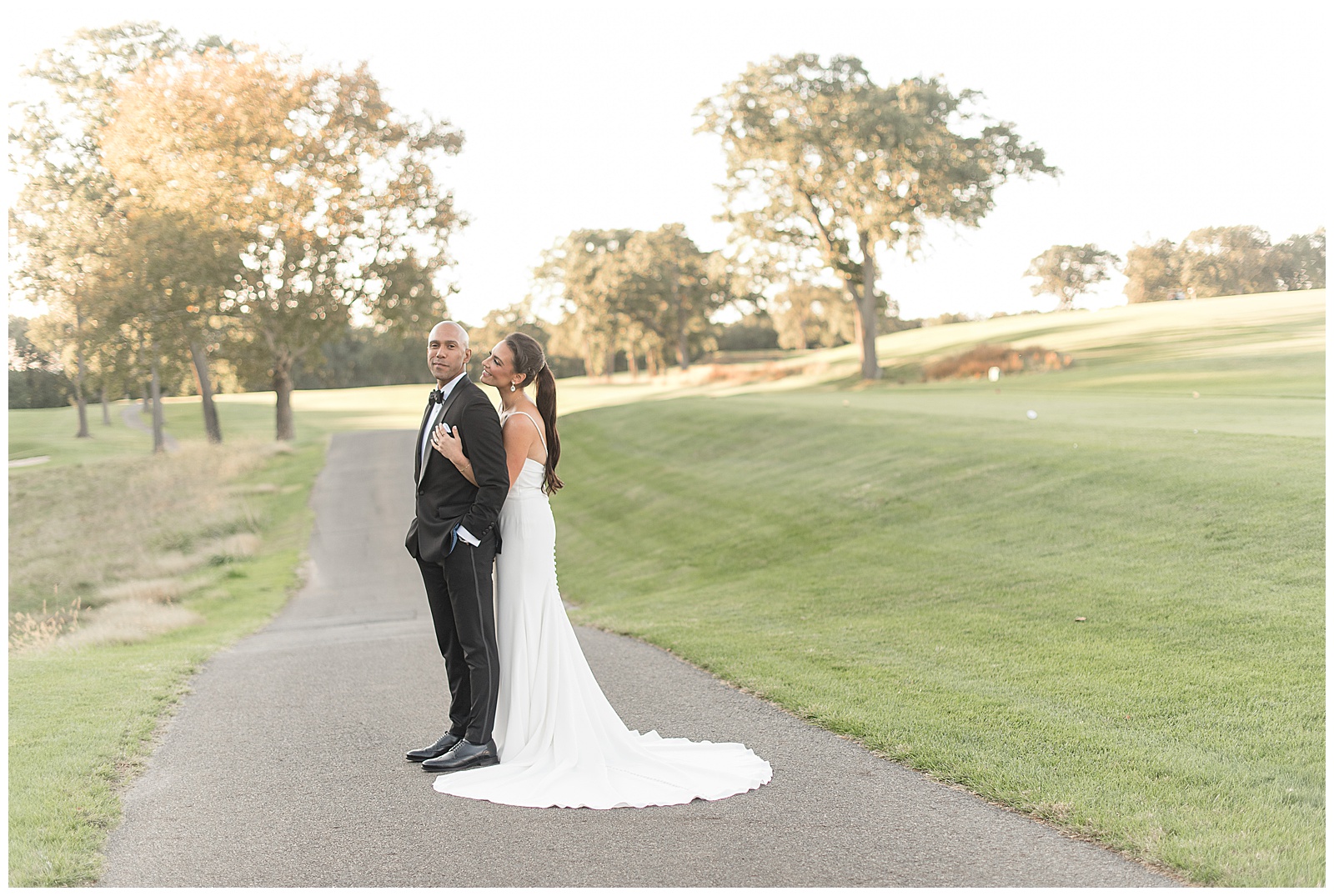 bride hugging groom from behind and looking at him as he looks at camera on golf course in northern new jersey