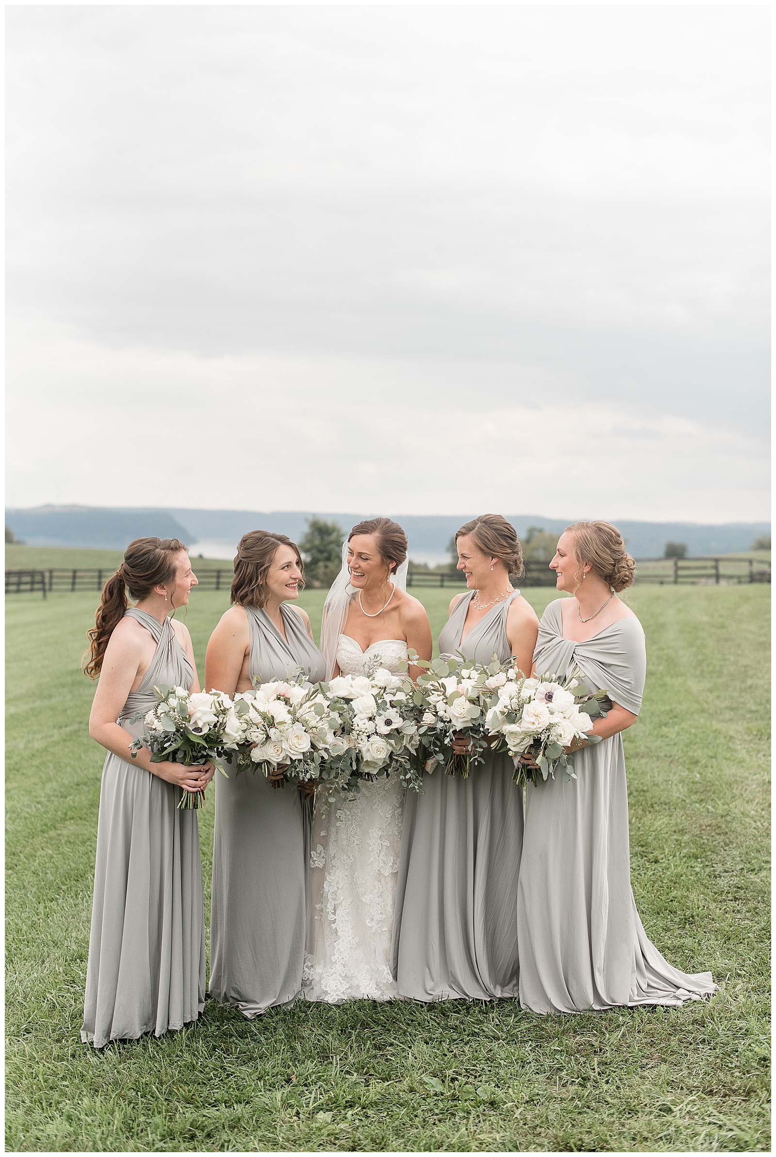bride in white strapless dress with bridesmaids wearing gray long dresses looking at each other at lauxmont farms