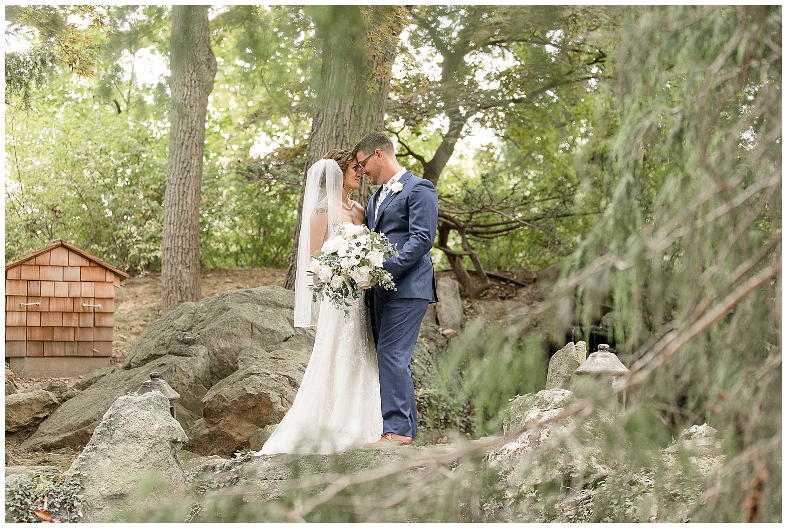 bride and groom standing close together on large rocks with foreheads touching surrounded by trees at lauxmont farms