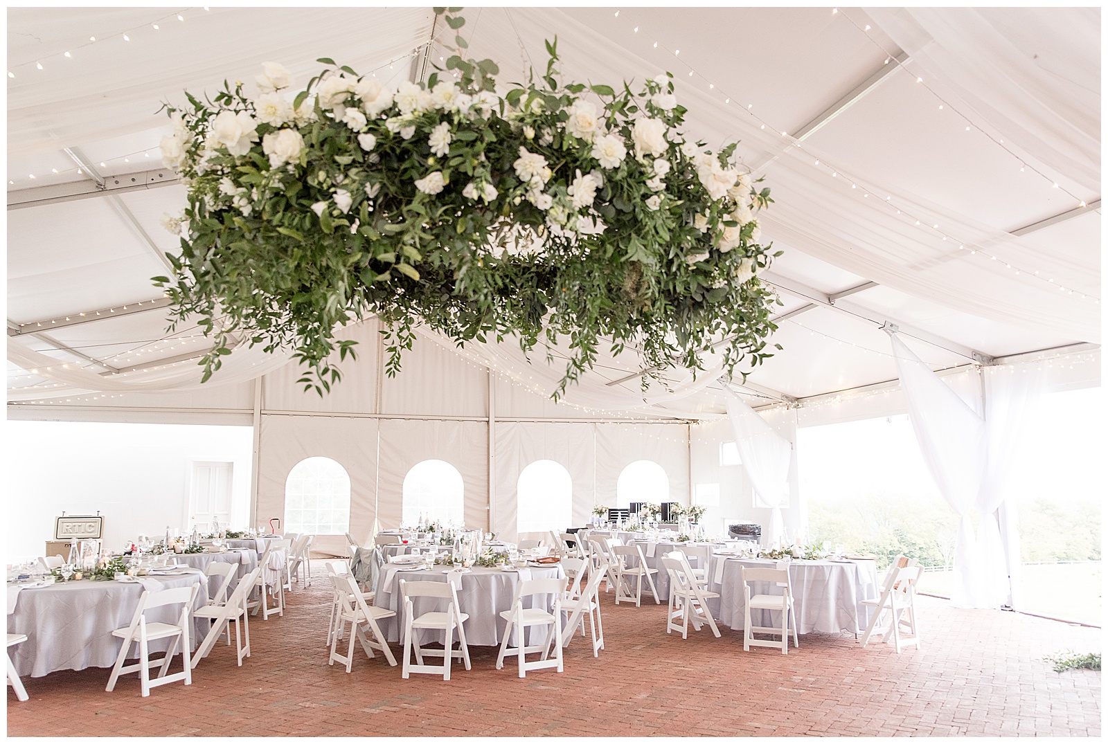 white tent reception decorated with white tables and chairs and huge floral masterpiece hanging from ceiling at lauxmont farms