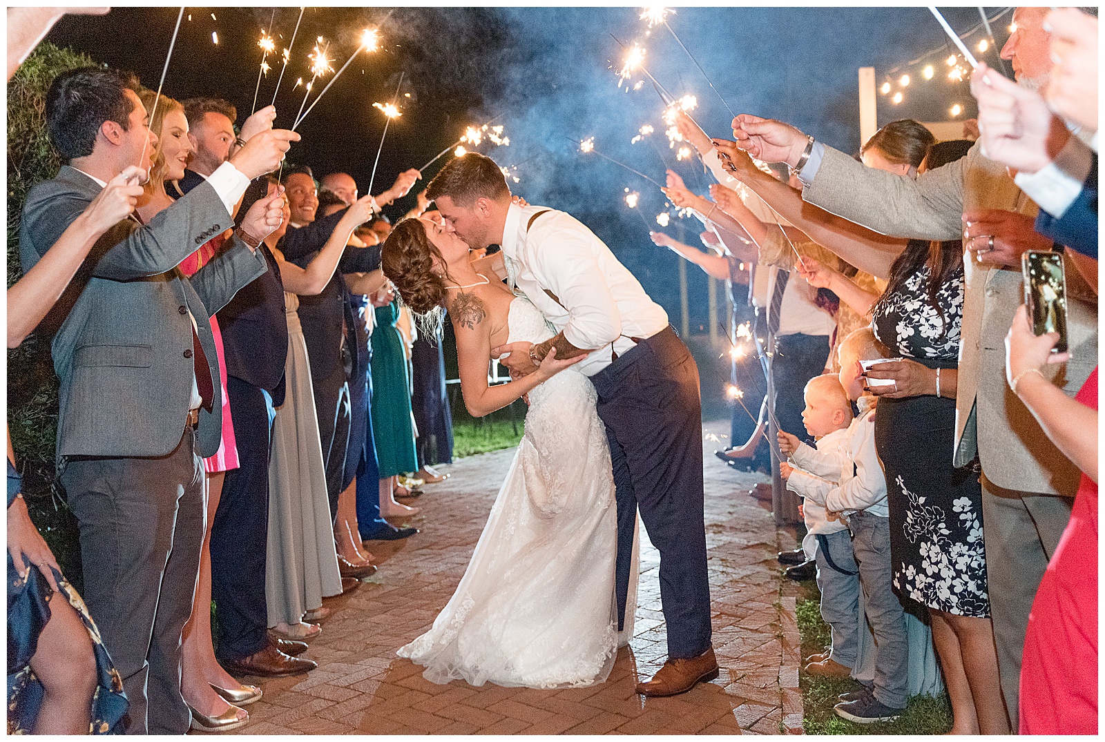 groom dipping bride back as they kiss leaving reception surrounded by guests holding sparklers at lauxmont farms in york pennsylvania