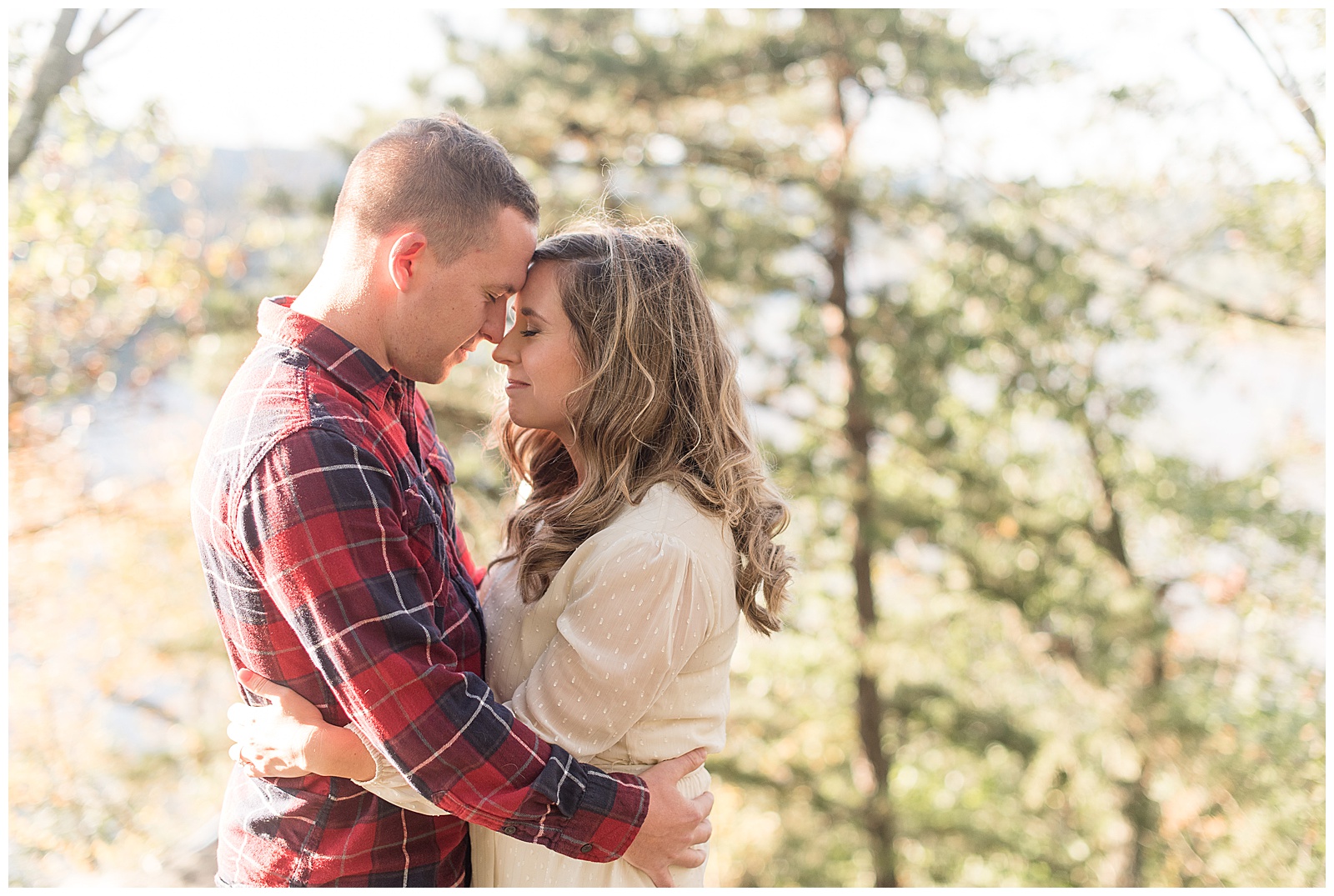 engaged couple hugging with their foreheads touching and their eyes closed with bright trees behind them at pinnacle point in holtwood pennsylvania