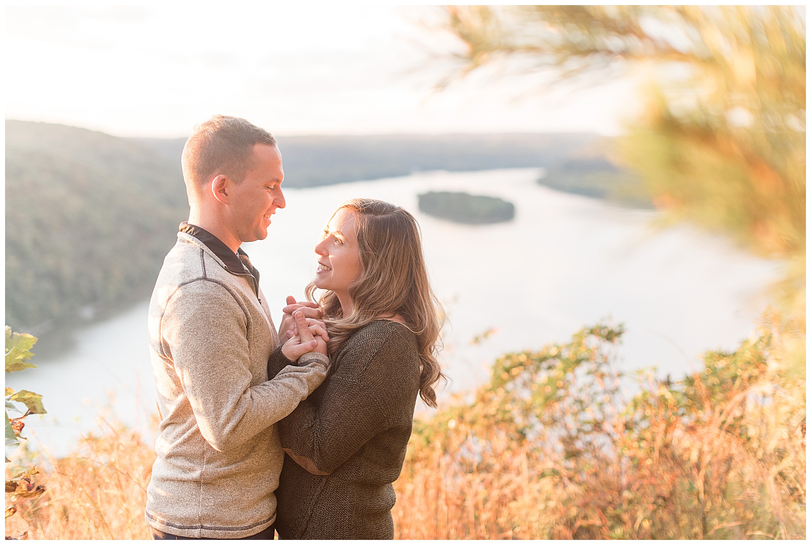 engaged couple standing close with their hands held between them as they smile and look at each other on fall day at pinnacle overlook in pennsylvania