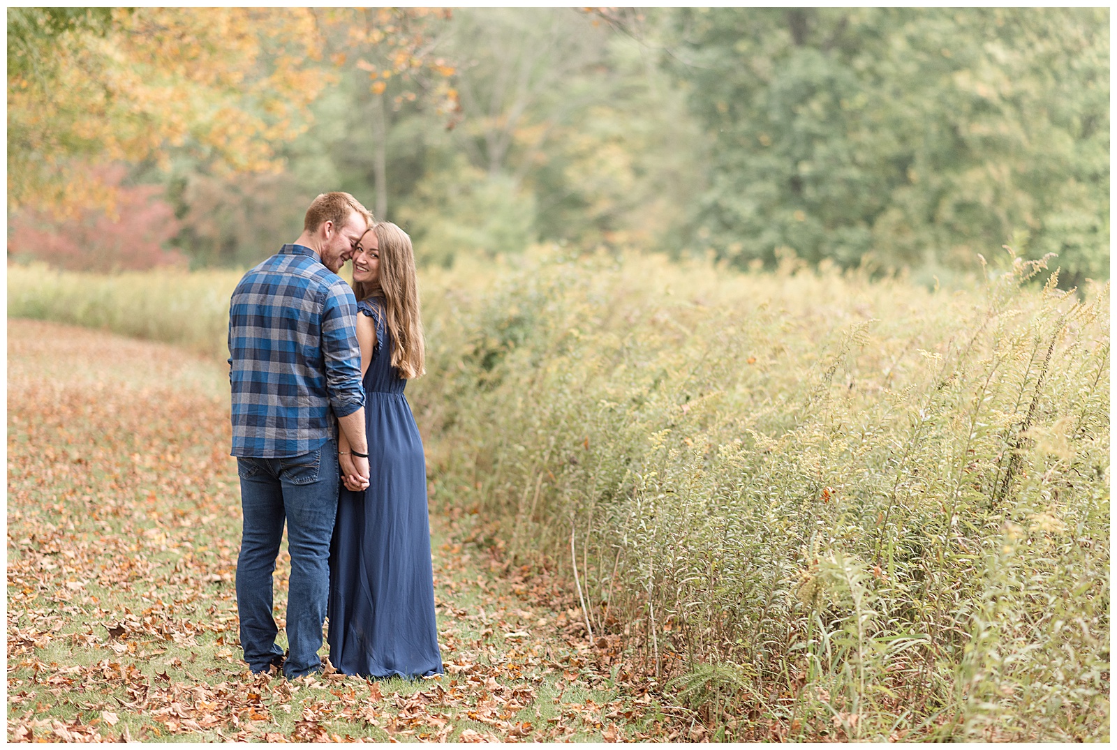 engaged couple with their backs toward camera standing close together by tall wild grasses on cloudy fall day at middle creek wildlife