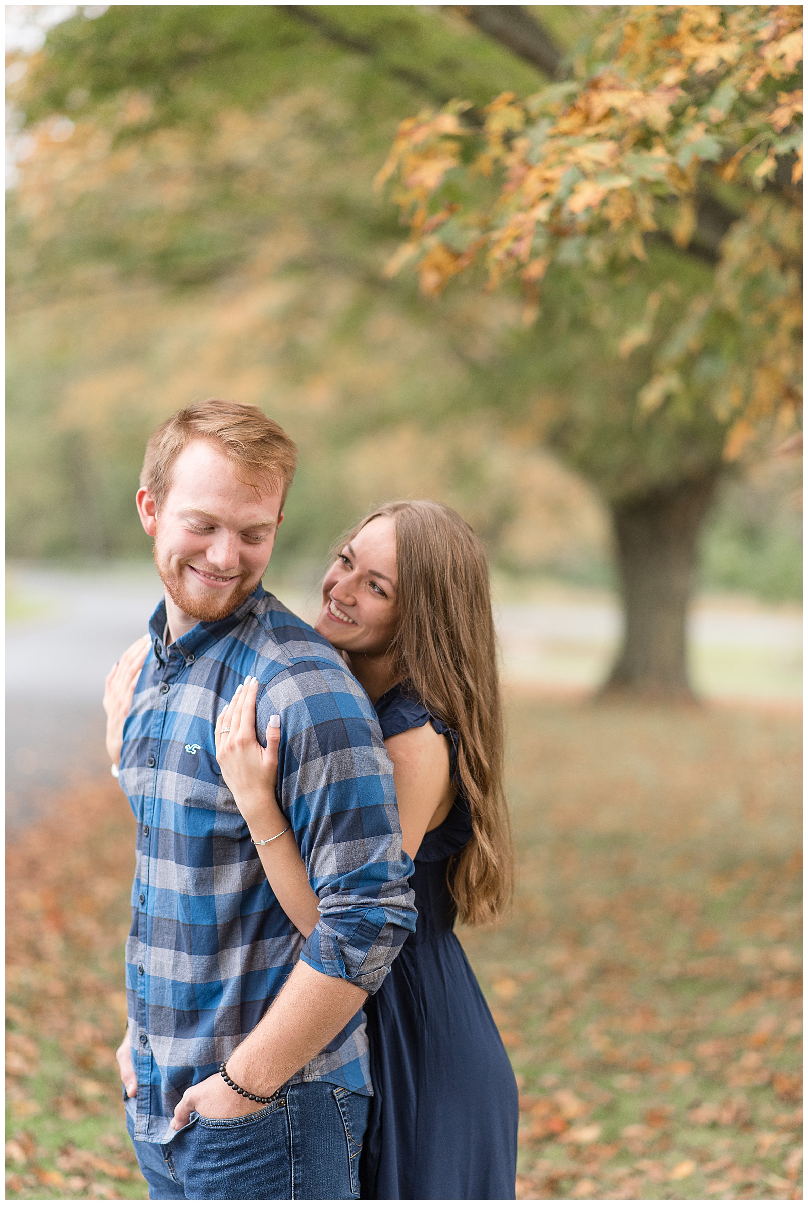 girl hugging guy from behind as he looks back and smiles surrounded by trees with their leaves beginning to change colors in lancaster pennsylvania