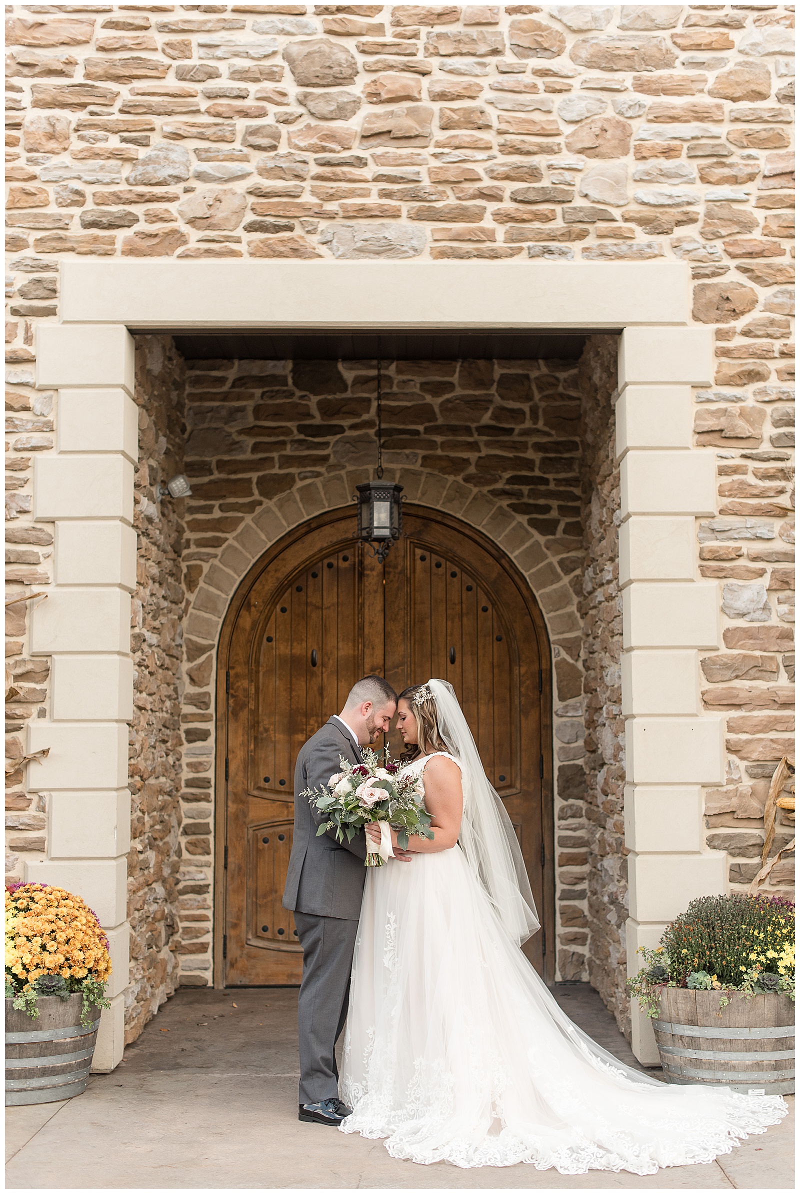 groom and bride standing close with their foreheads touching as bride holds bouquet by entrance to folino estate