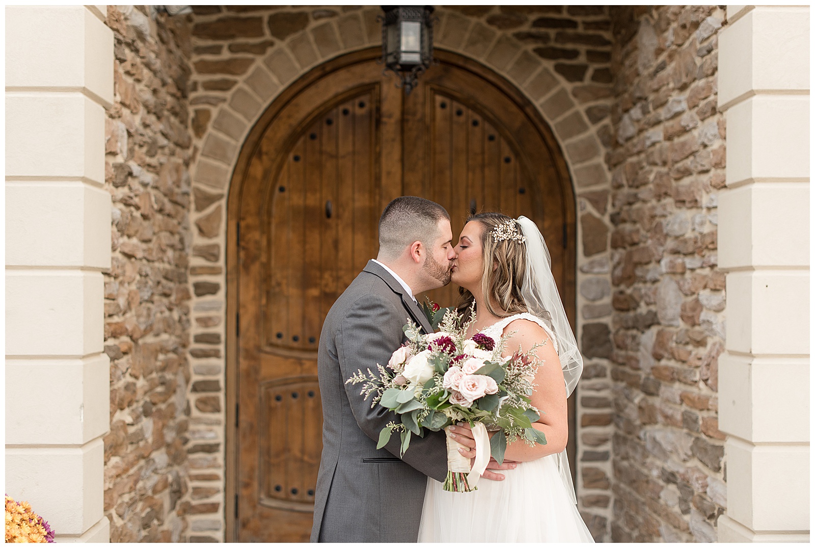 bride and groom kissing outside entrance to folino estate as bride holds beautiful bouquet in kutztown pennsylvania