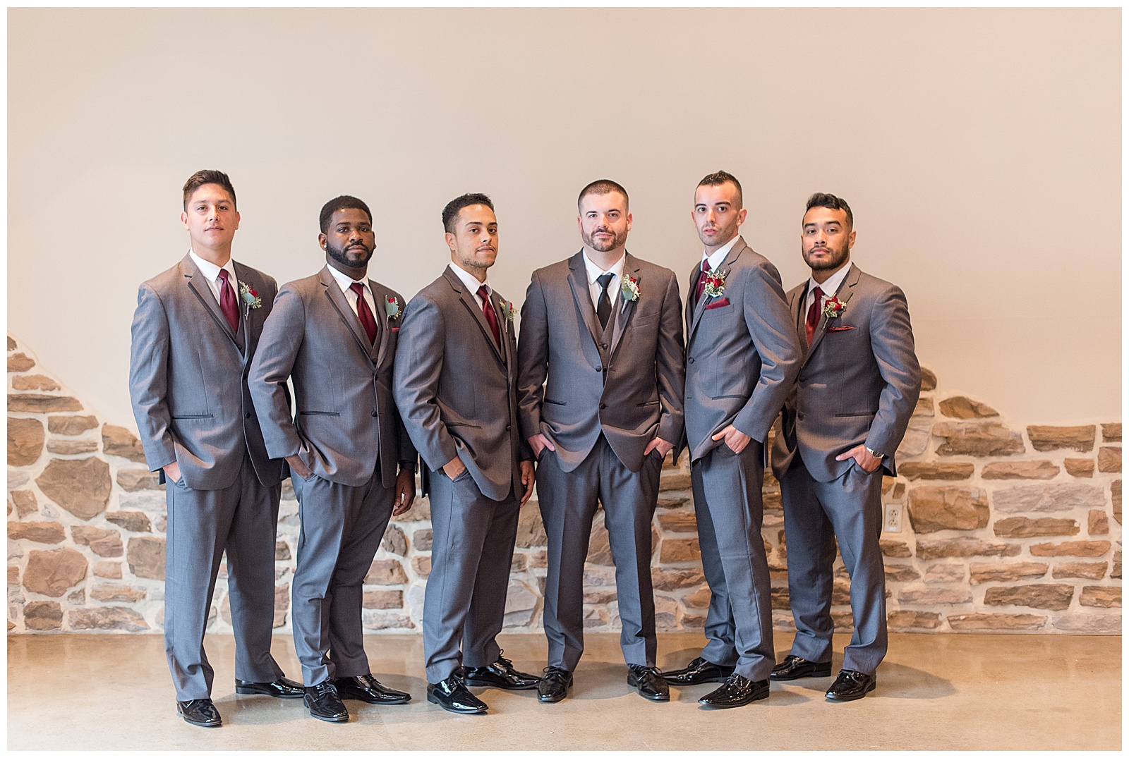 groom surrounded by his five groomsmen all in dark gray suits with their hands in their pockets by stone wall at folino estate