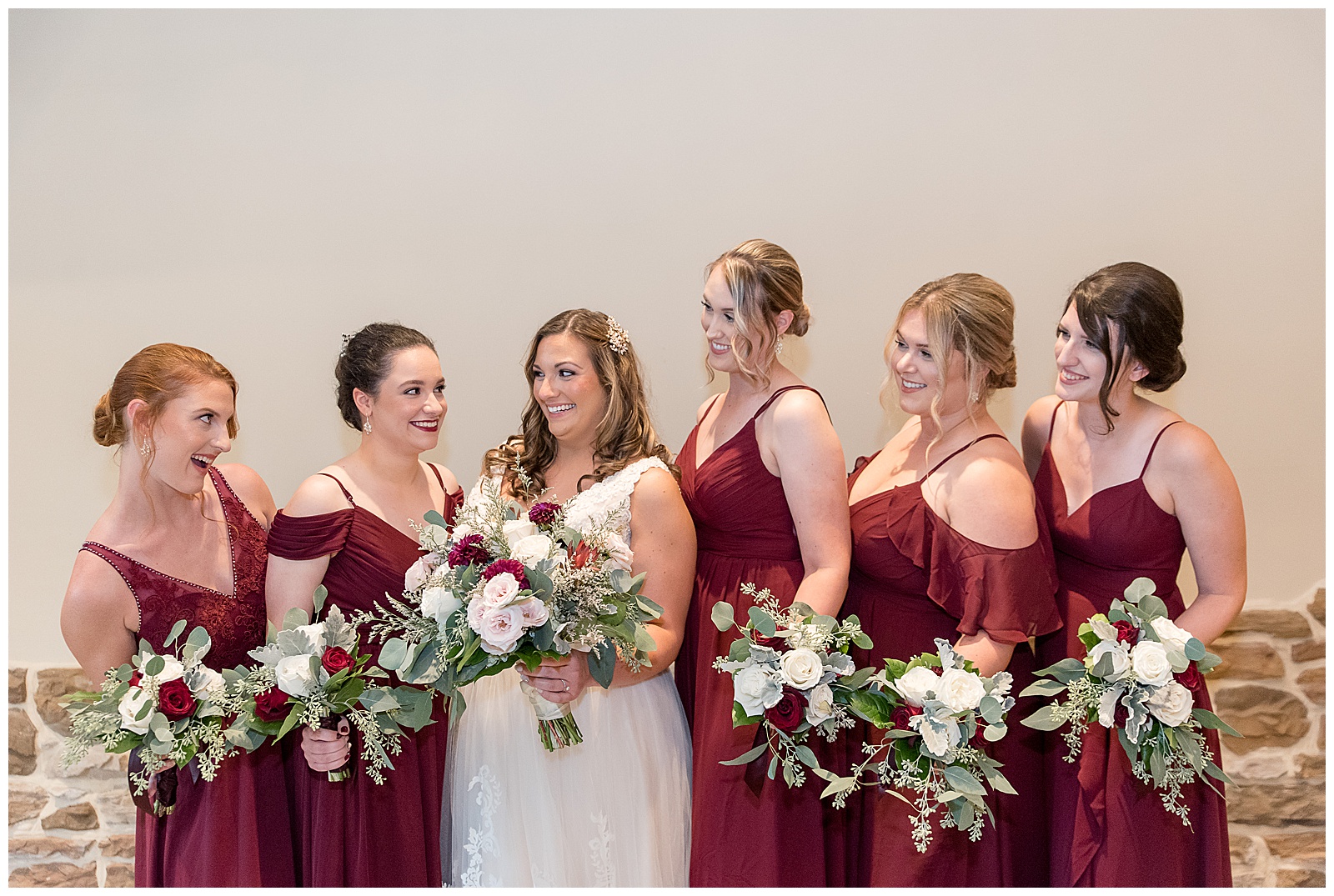 bride with her bridesmaids standing close together all smiling at the bride and holding red and white bouquets at folino estate
