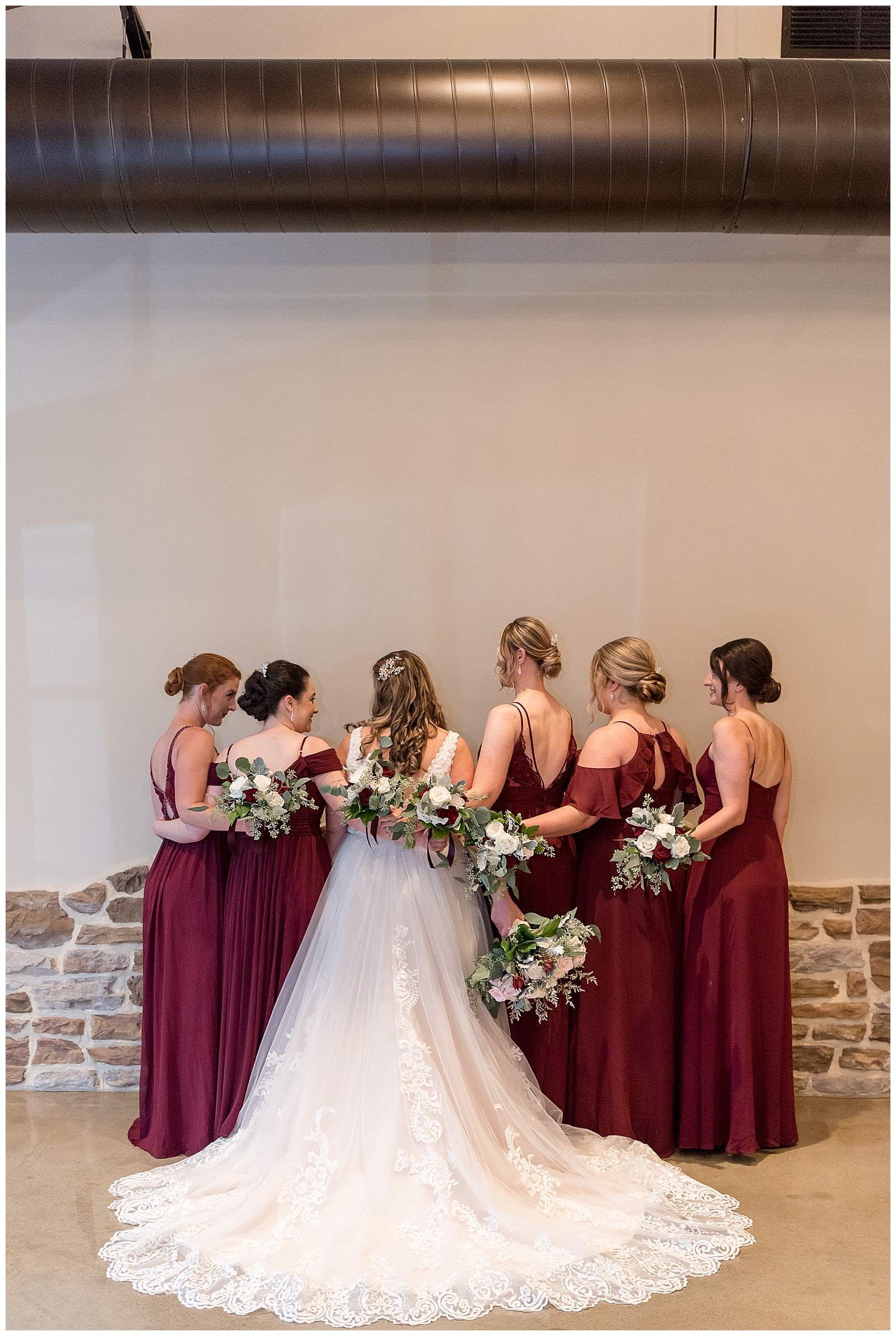 backs of bride and her bridesmaids toward camera with their arms wrapped around each other inside folino estate
