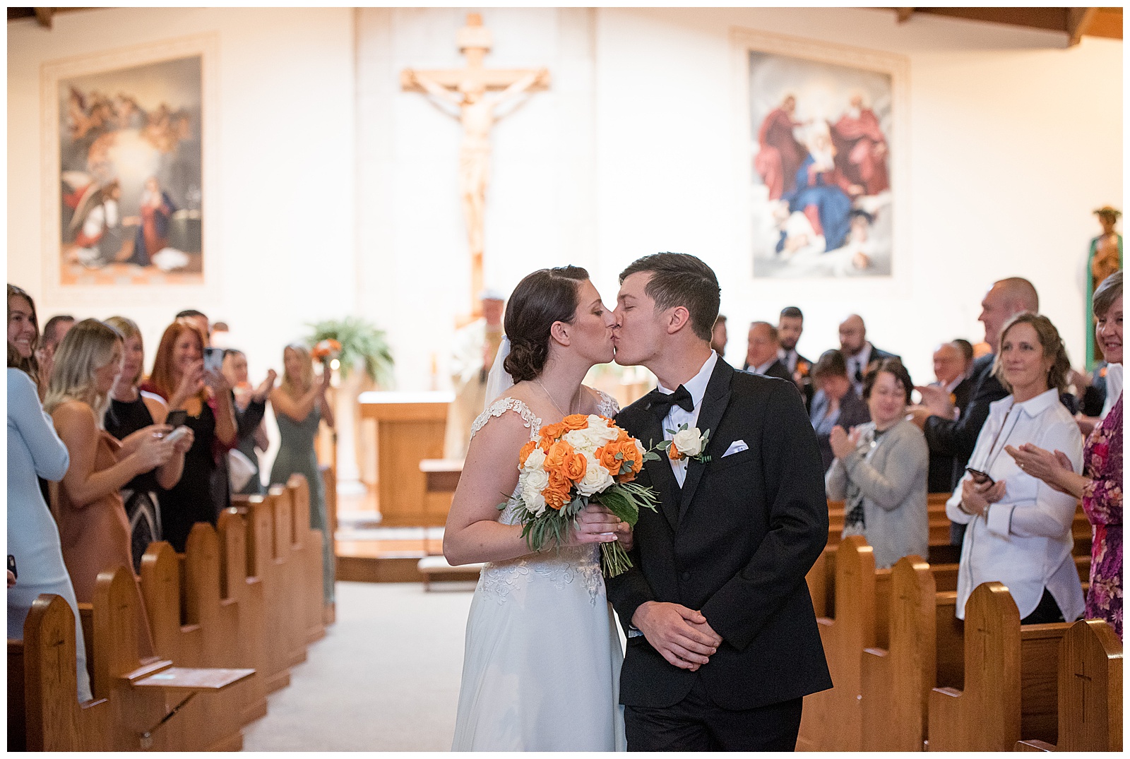bride and groom kissing at the end of aisle as they're leaving wedding ceremony and guests are turned around watching them in collegeville pennsylvania