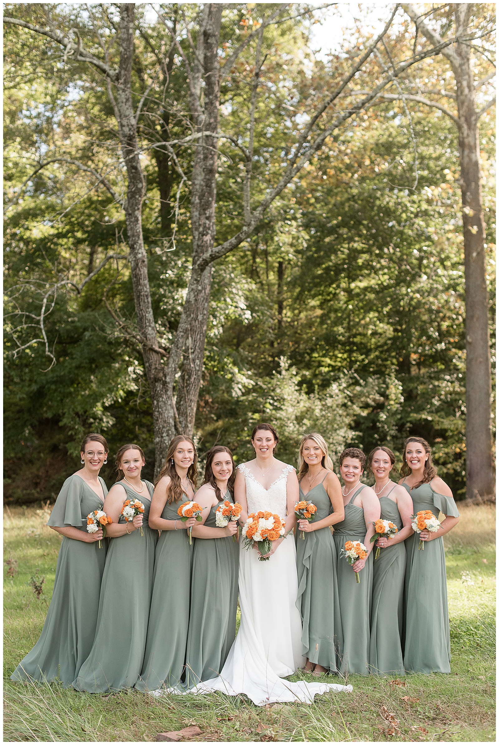 bride surrounded by her eight bridesmaids wearing muted green floor-length gowns holding bouquets in montgomery county pennsylvania