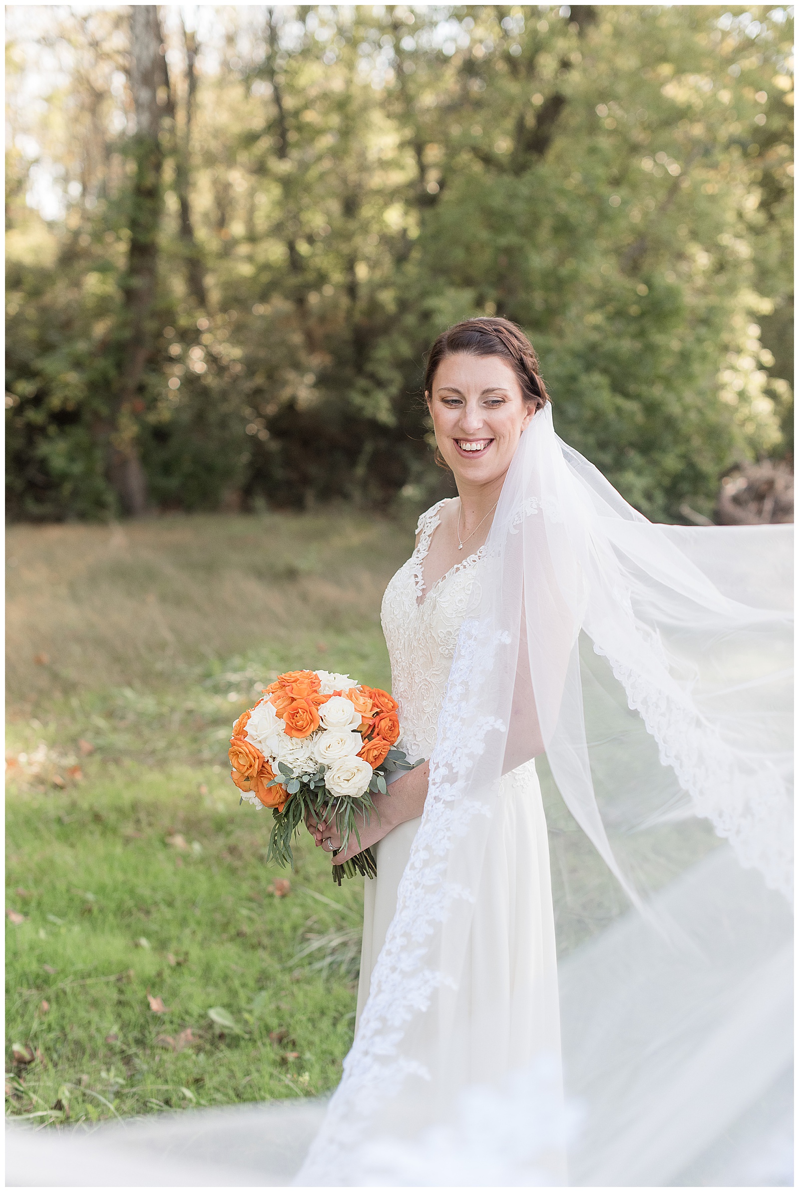 bride holding bouquet and surrounded by her blowing veil as she looks down and smiles in collegeville pennsylvania
