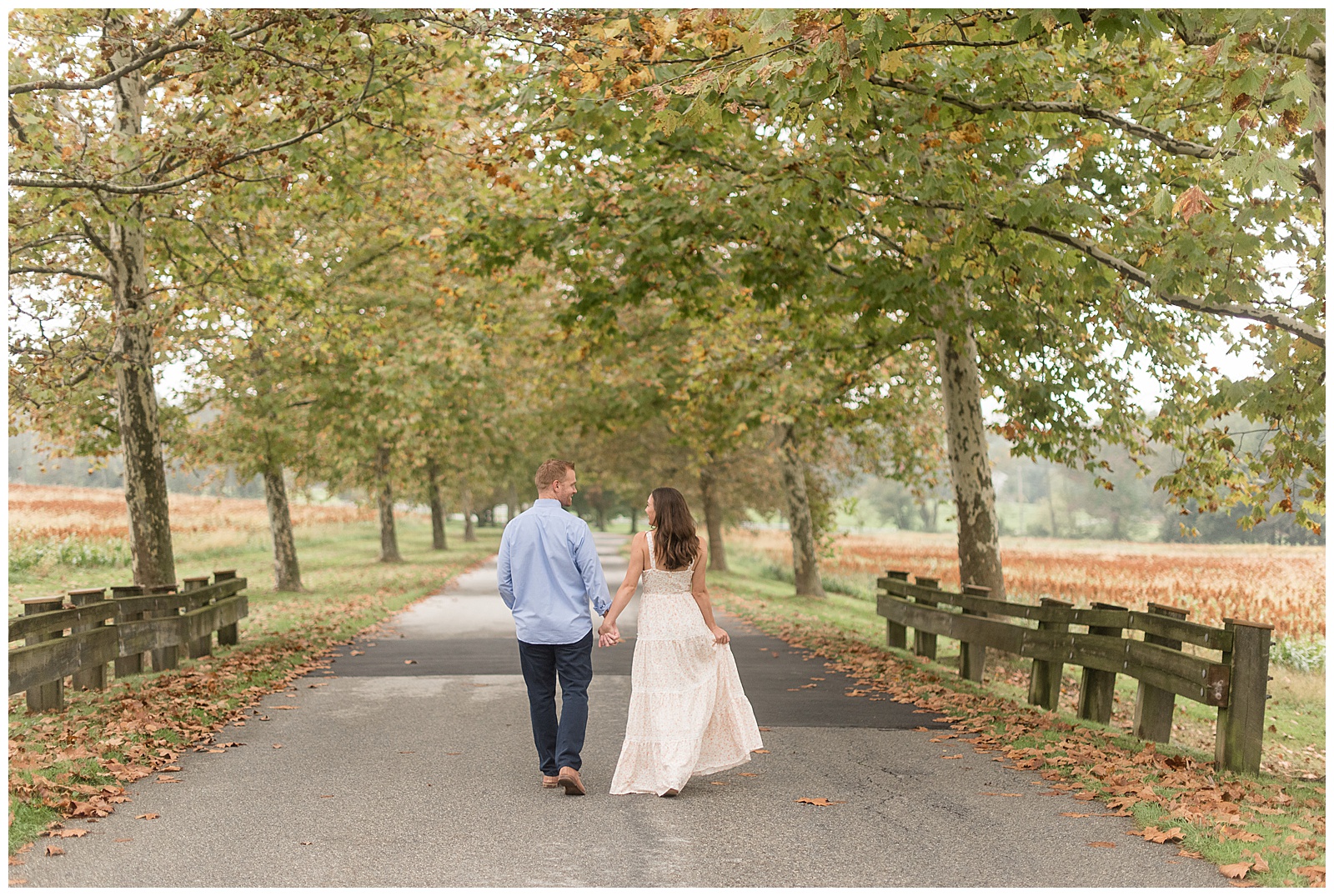 engaged couple holding hands walking on stone pathway away from camera as they look at each other at springton manor farms