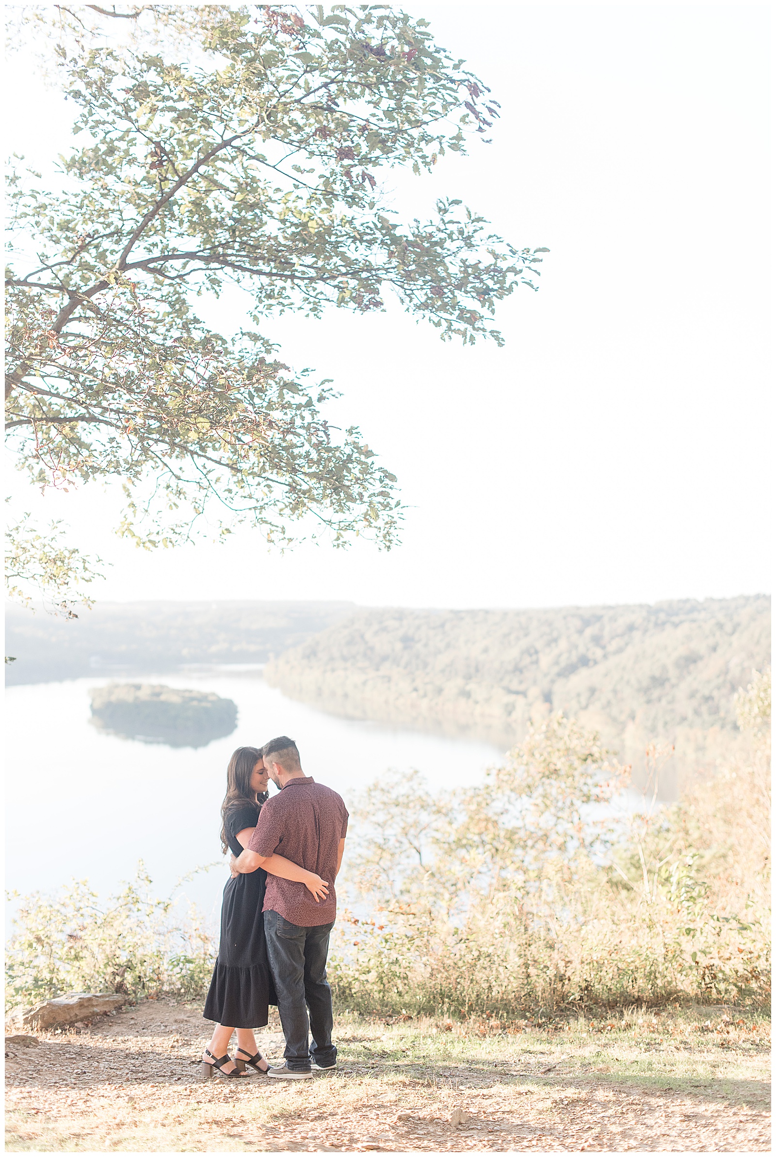 engaged couple hugging tightly at pinnacle point overlook with susquehanna river behind them on bright fall day in lancaster county