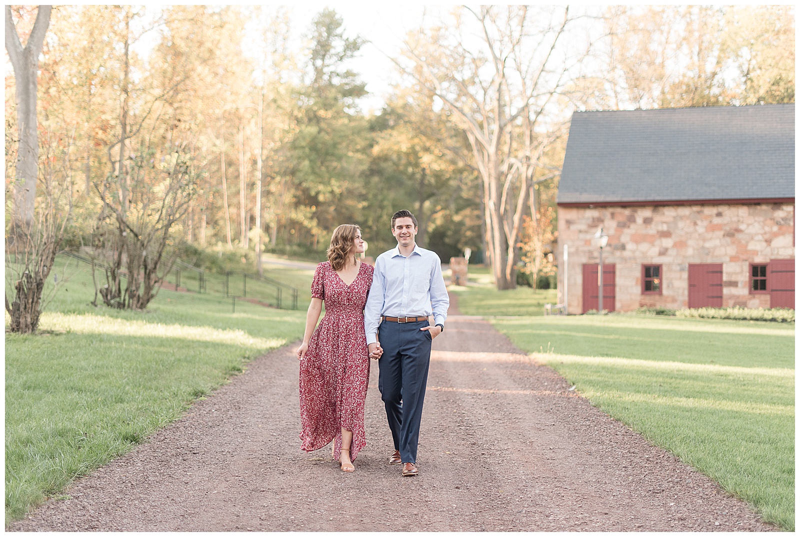engaged couple holding hands walking towards camera and guy smiles and girl looks up at him holding her dress with right hand at elizabeth furnace